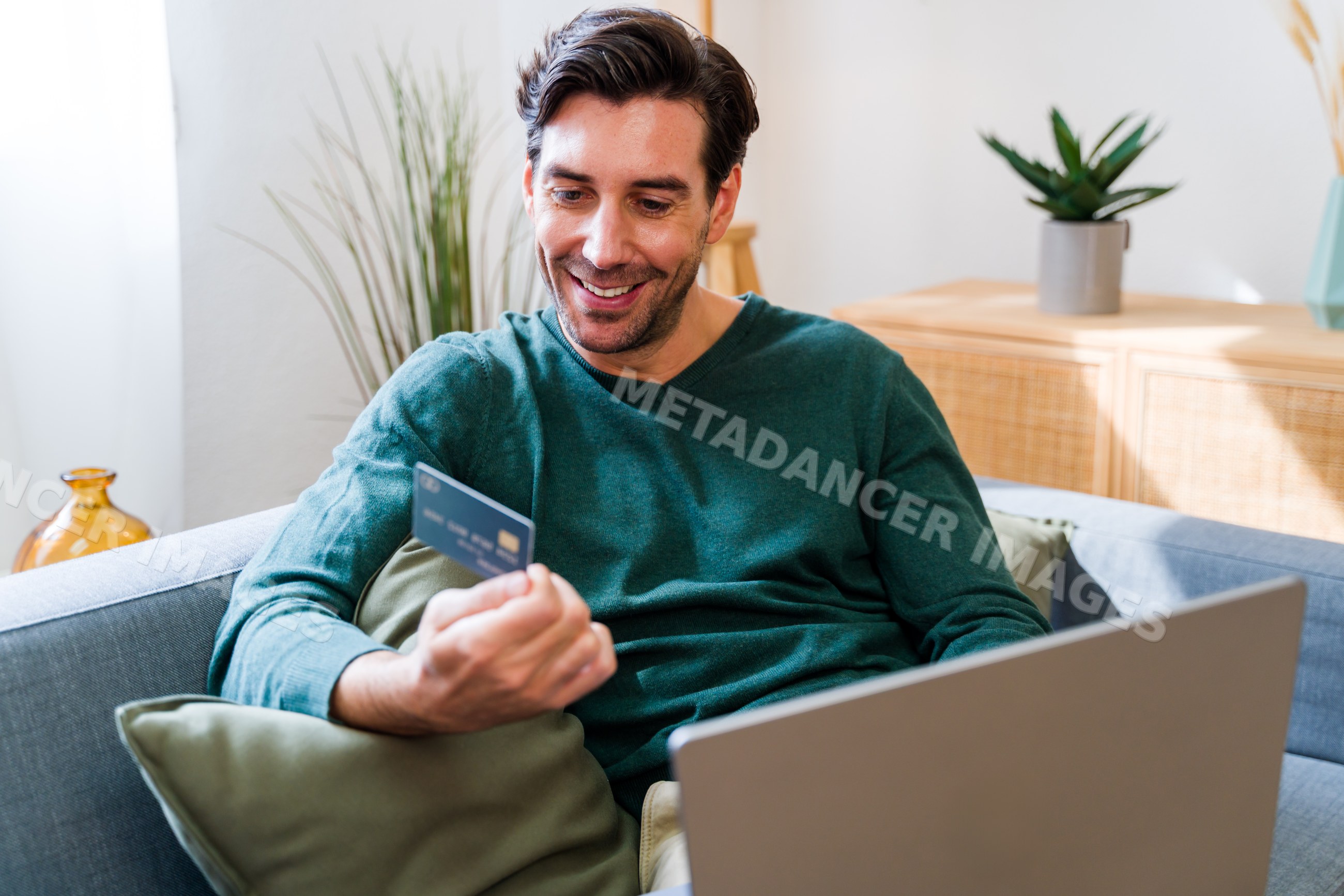White man holding credit card using laptop in living room