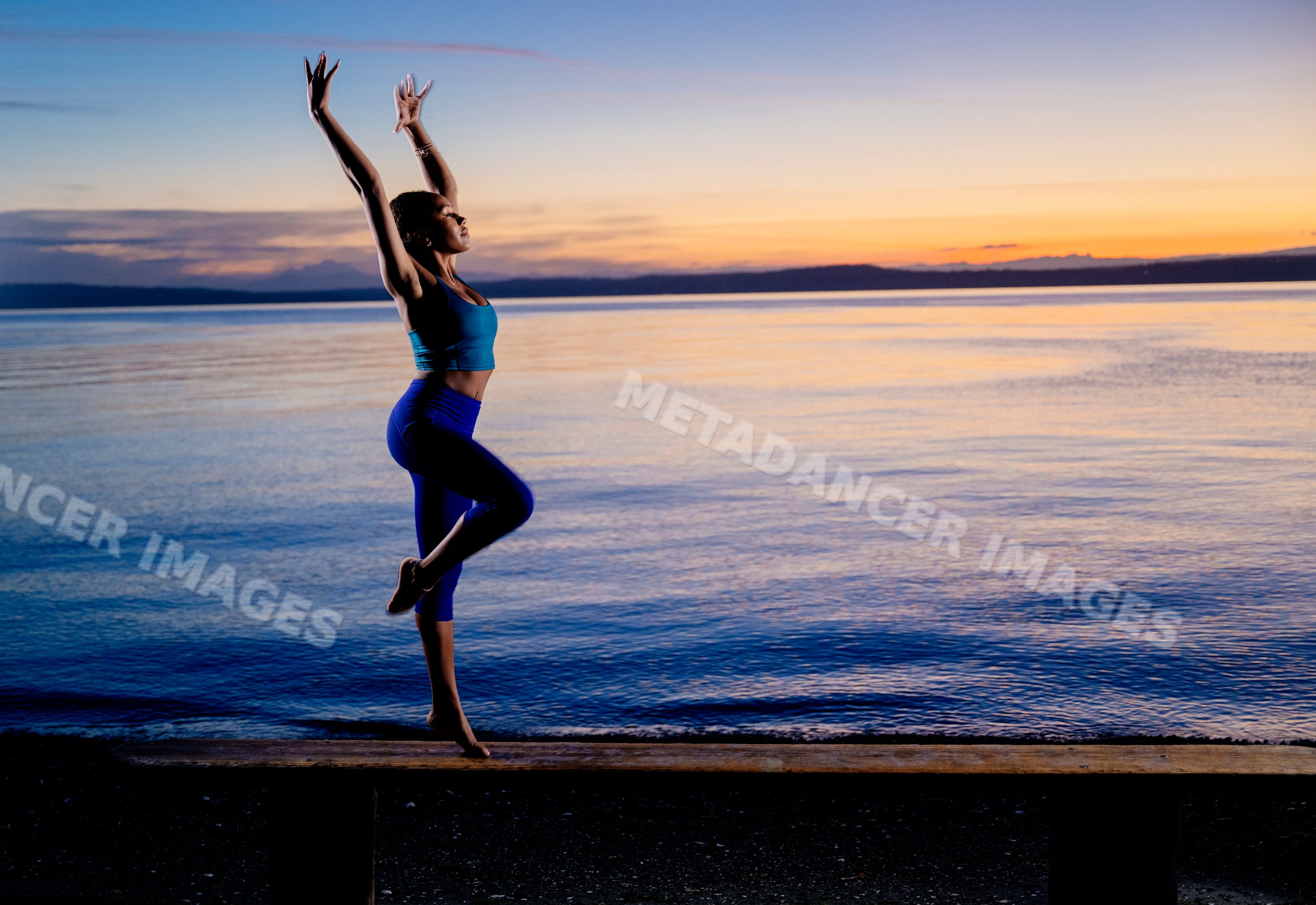 Hispanic woman practicing yoga balance pose on bench by lake at sunset