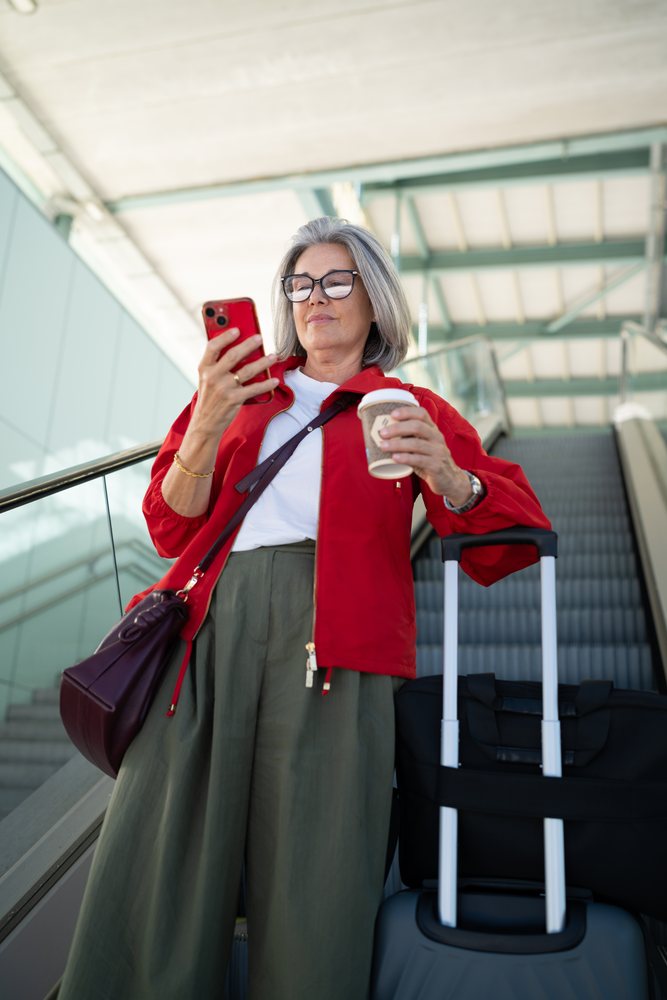 Middle-aged white woman with luggage checking phone on airport