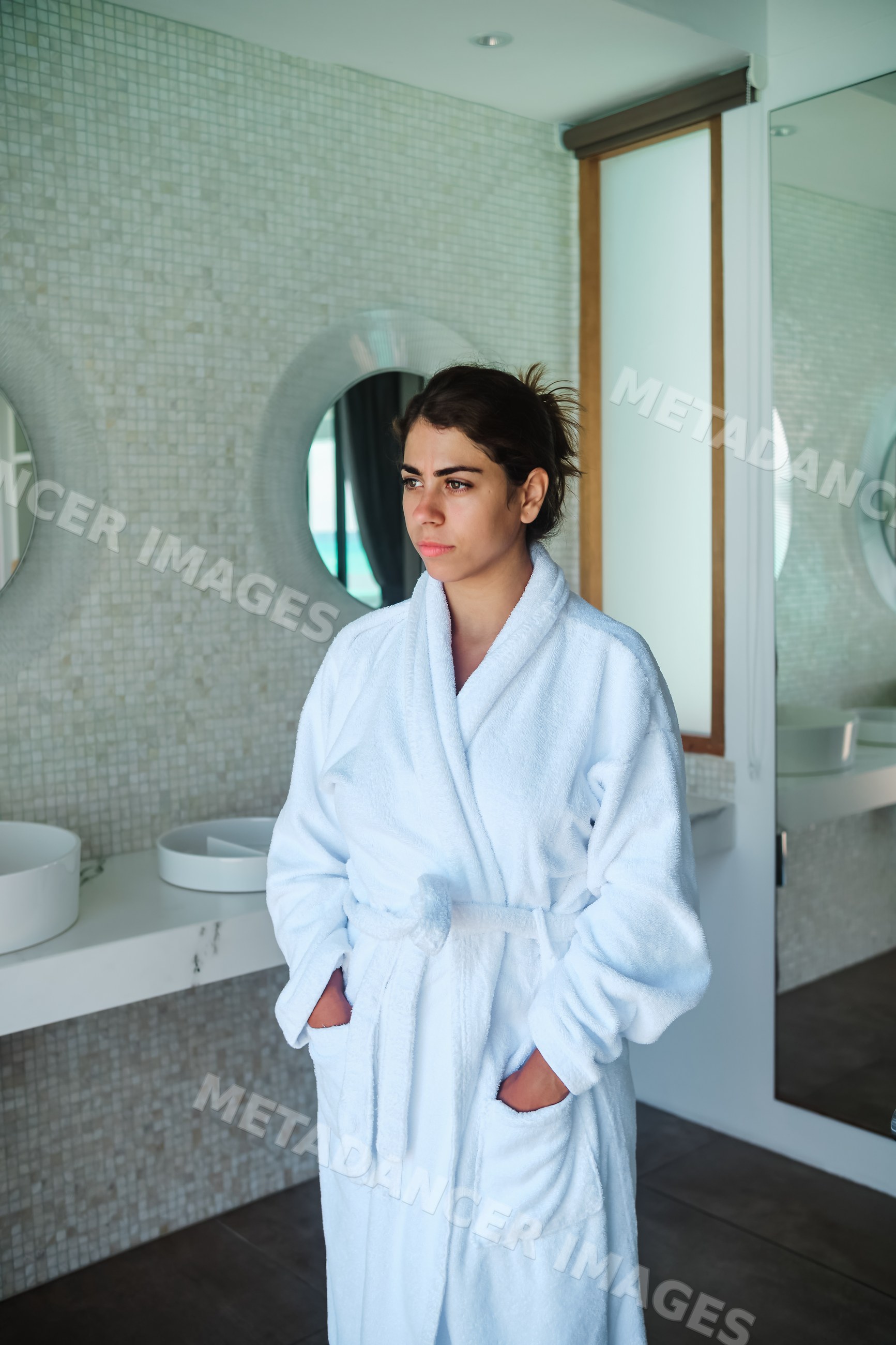 Woman wearing a white bathrobe standing in a modern bathroom interior