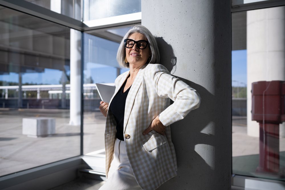 Businesswoman with laptop leans on a column inside modern building