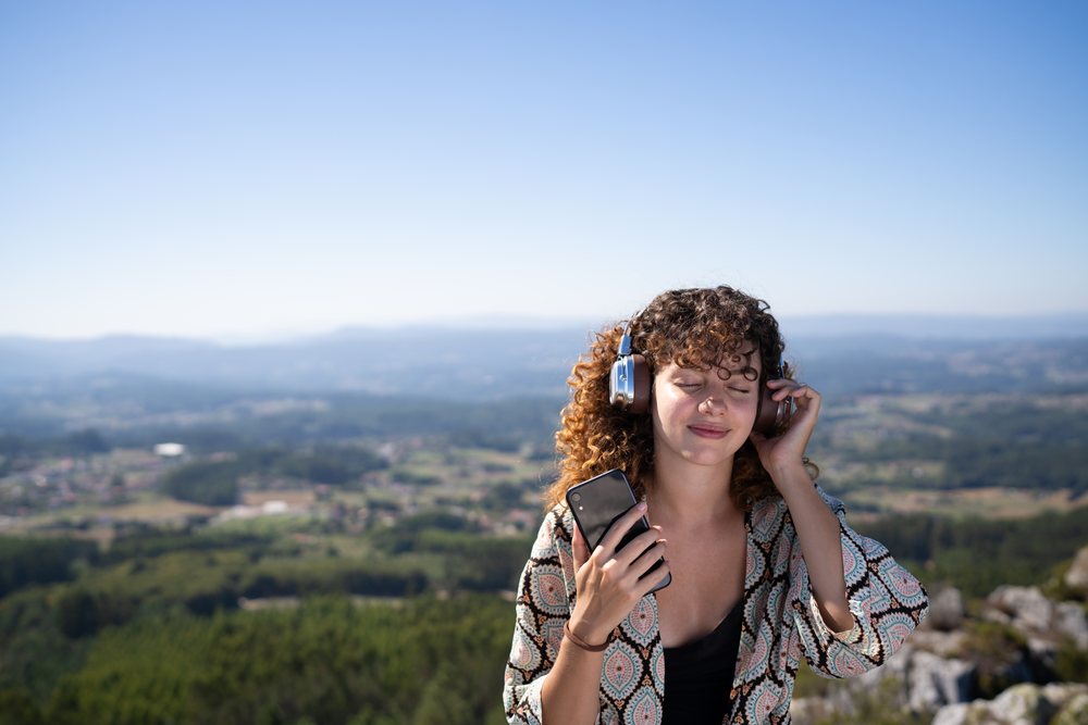 White woman enjoying music with headphones outdoors on mountain