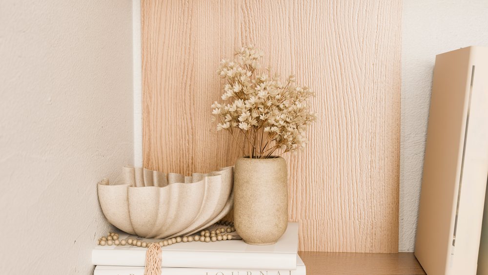 Beige vase with dried flowers and decorative bowl on books