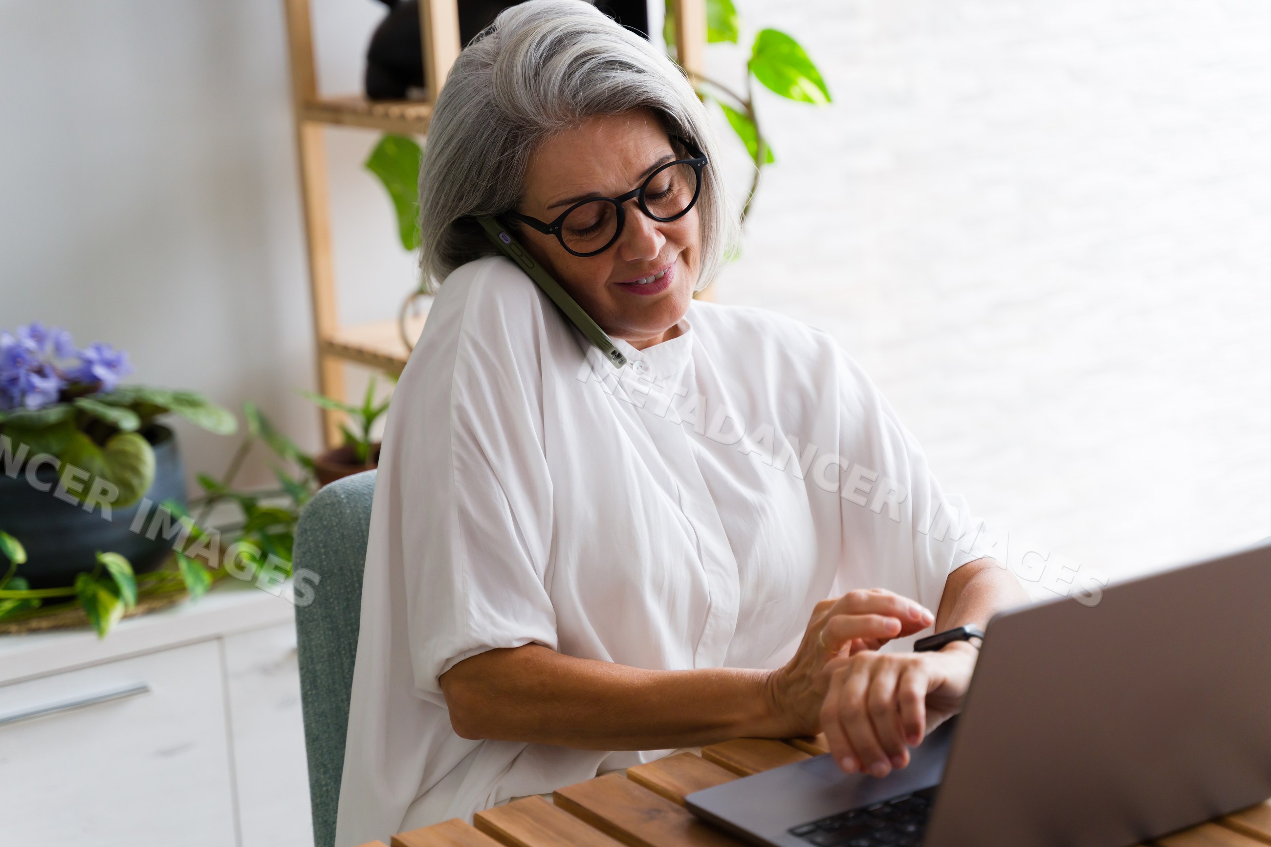 Mature white woman multitasking with phone smartwatch and laptop