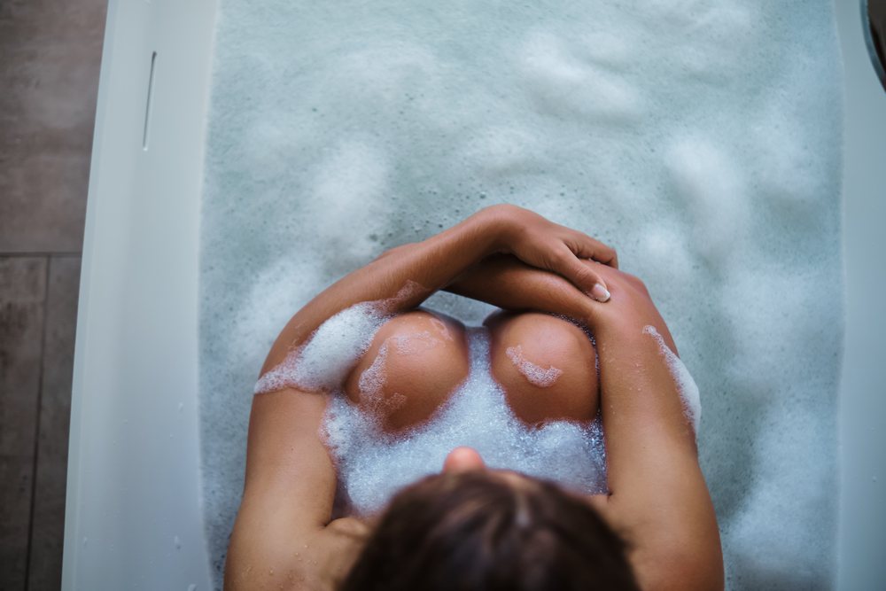 A white woman relaxes in a bubble bath in a bathtub