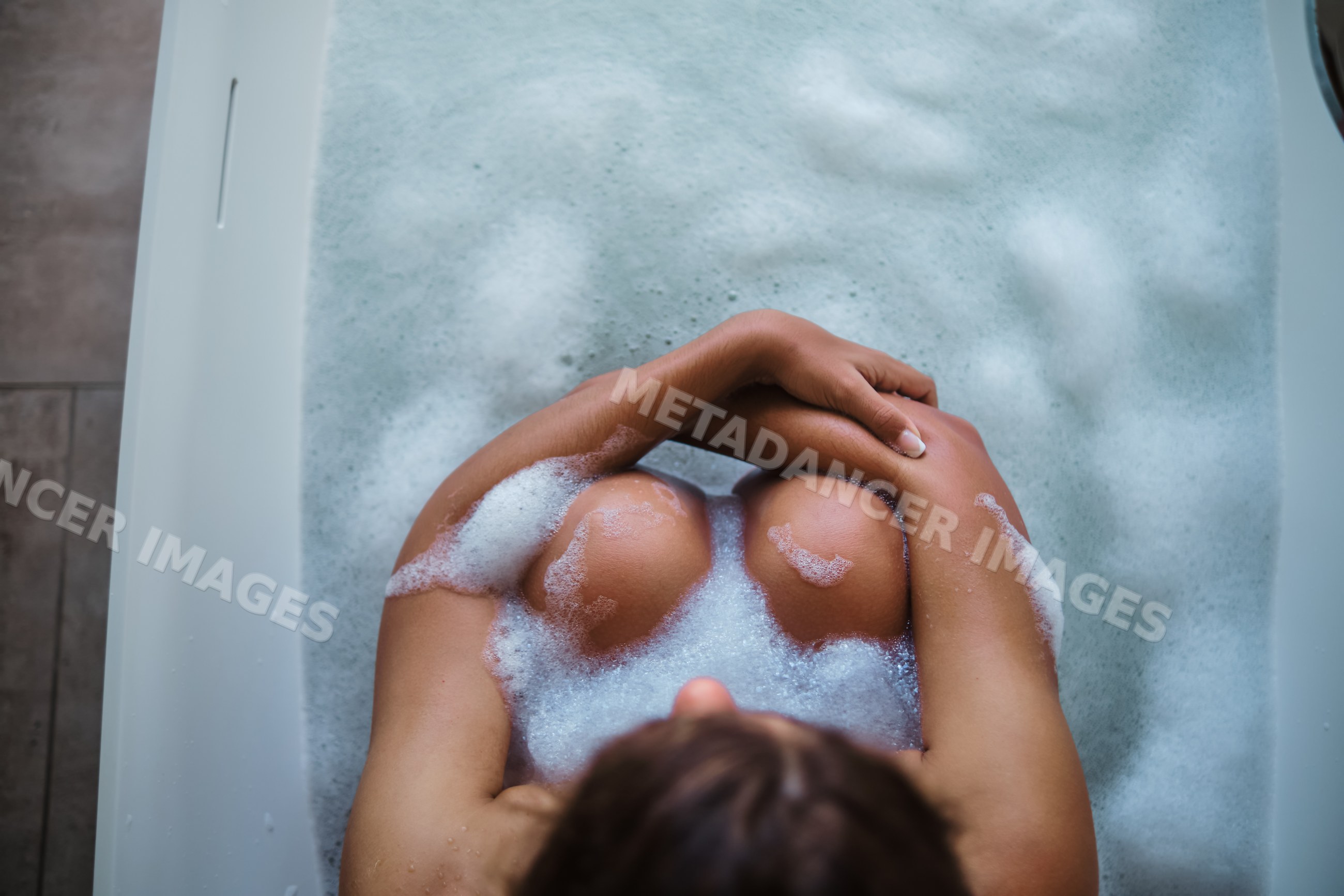 A white woman relaxes in a bubble bath in a bathtub