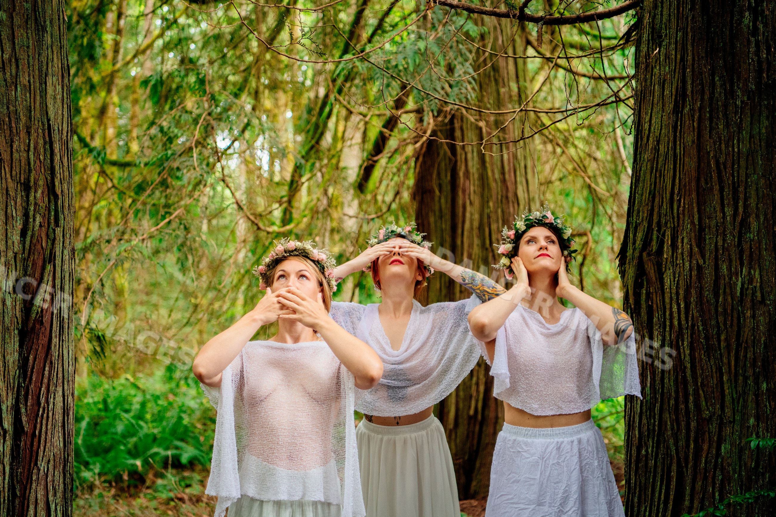 Three women in white with floral crowns in forest setting