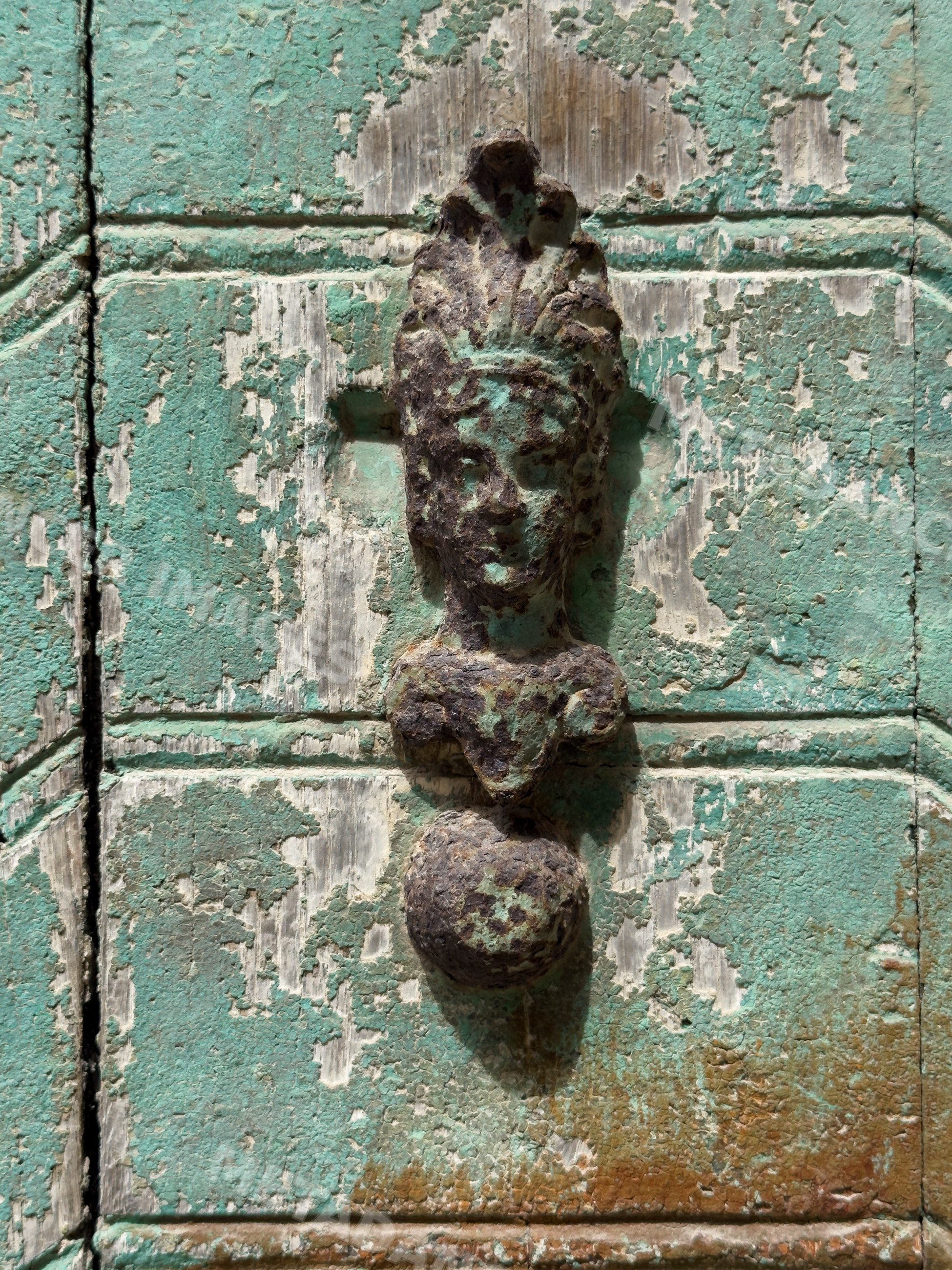 Weathered metal face-shaped door knocker on green door panel