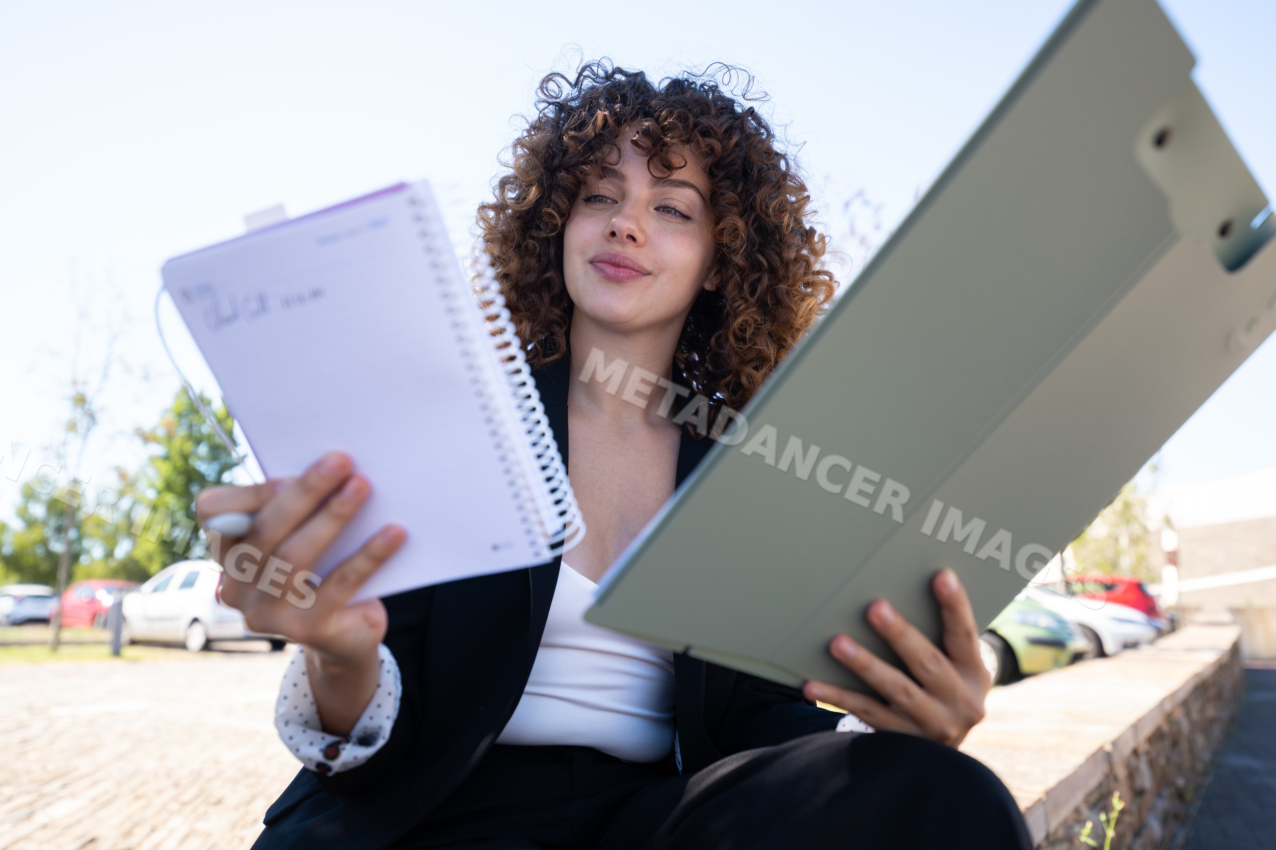 Businesswoman checking notes in spiral notebook outdoors