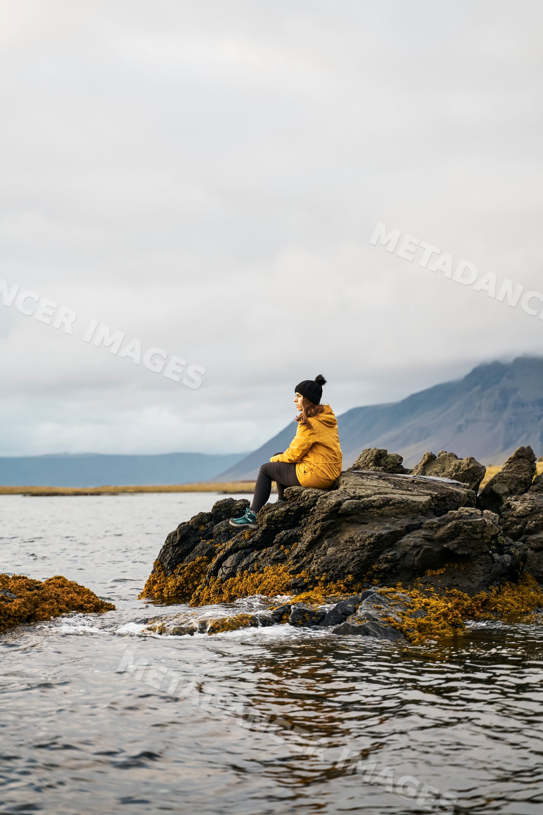 A white woman sitting on rocks by the water with mountains