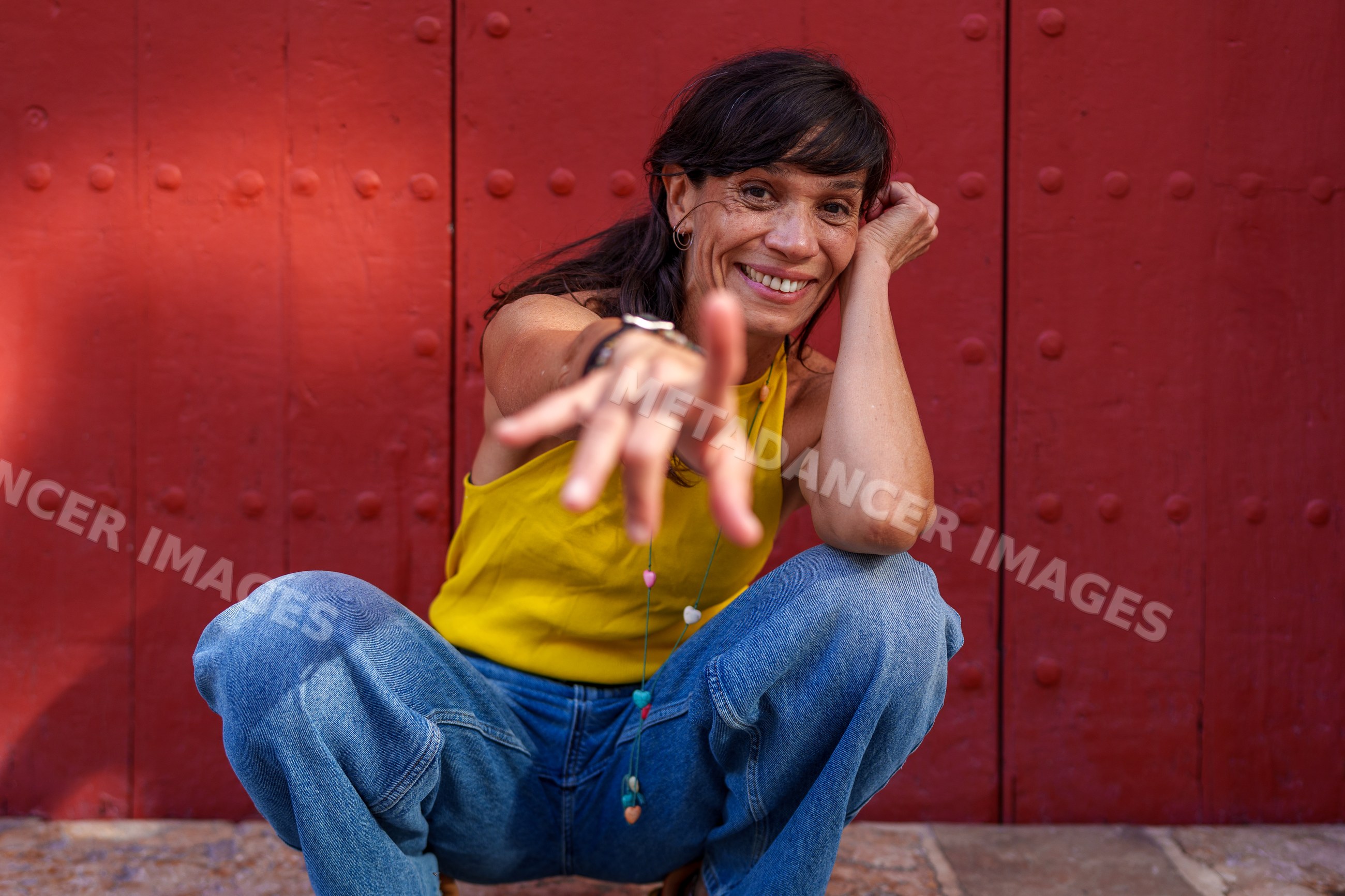 Hispanic woman crouching and reaching in front of red door outdoors