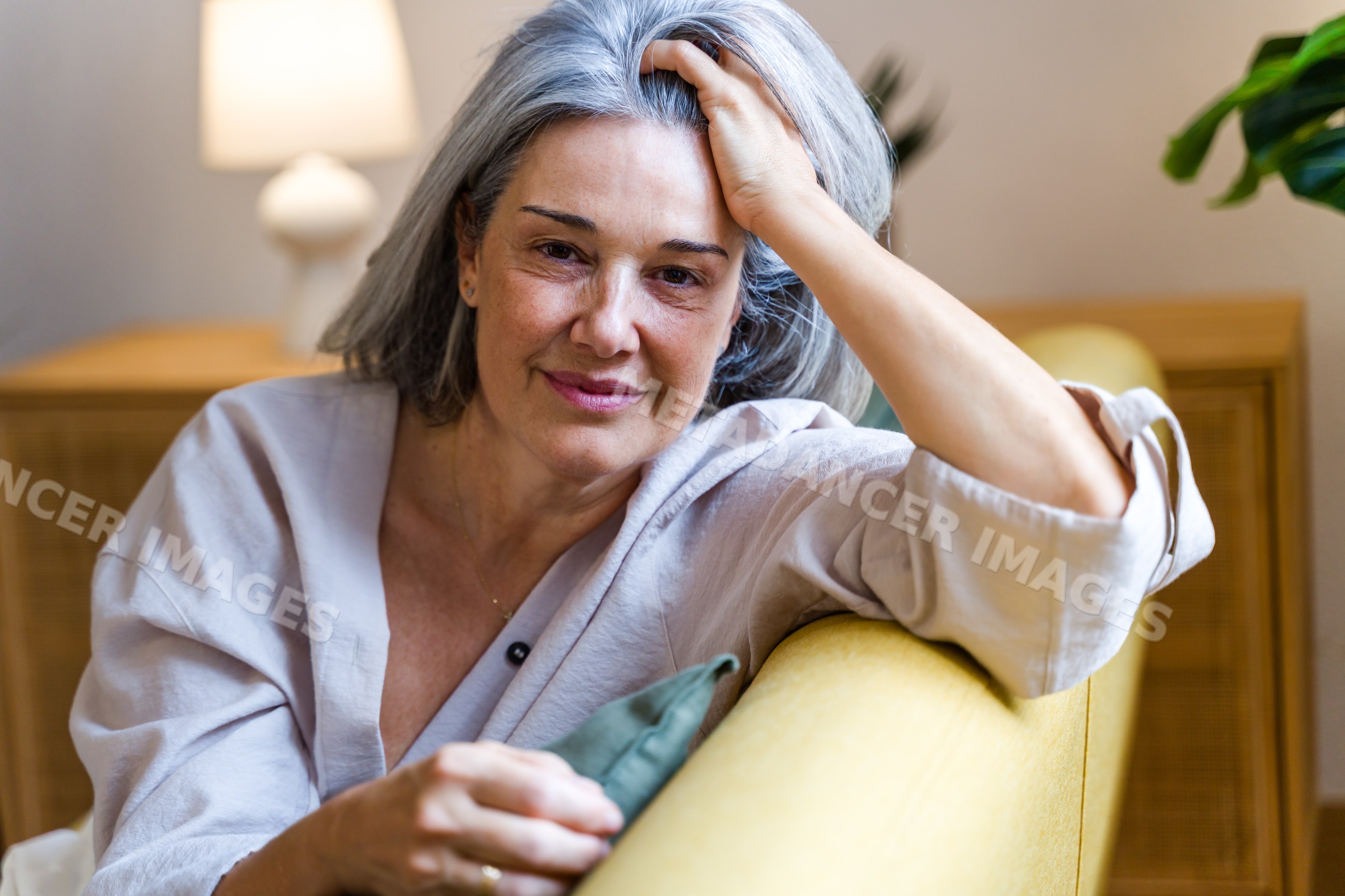 White woman with gray hair relaxing on yellow sofa indoors