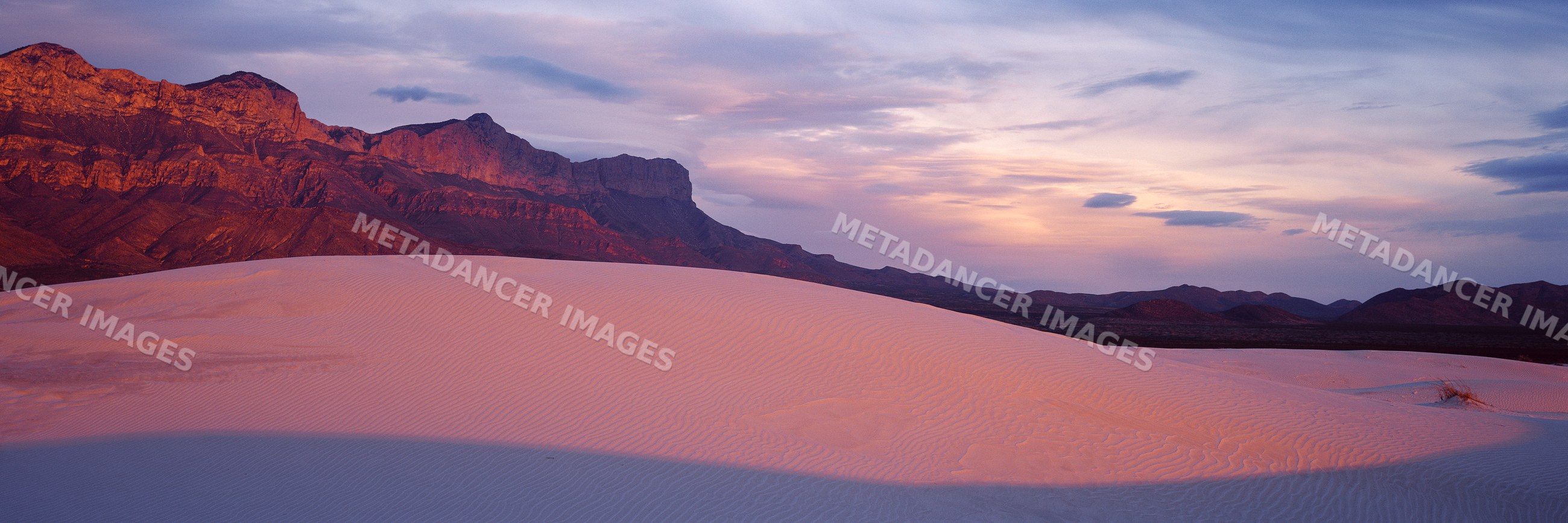 Sand dunes and desert mountains at sunset with dramatic sky