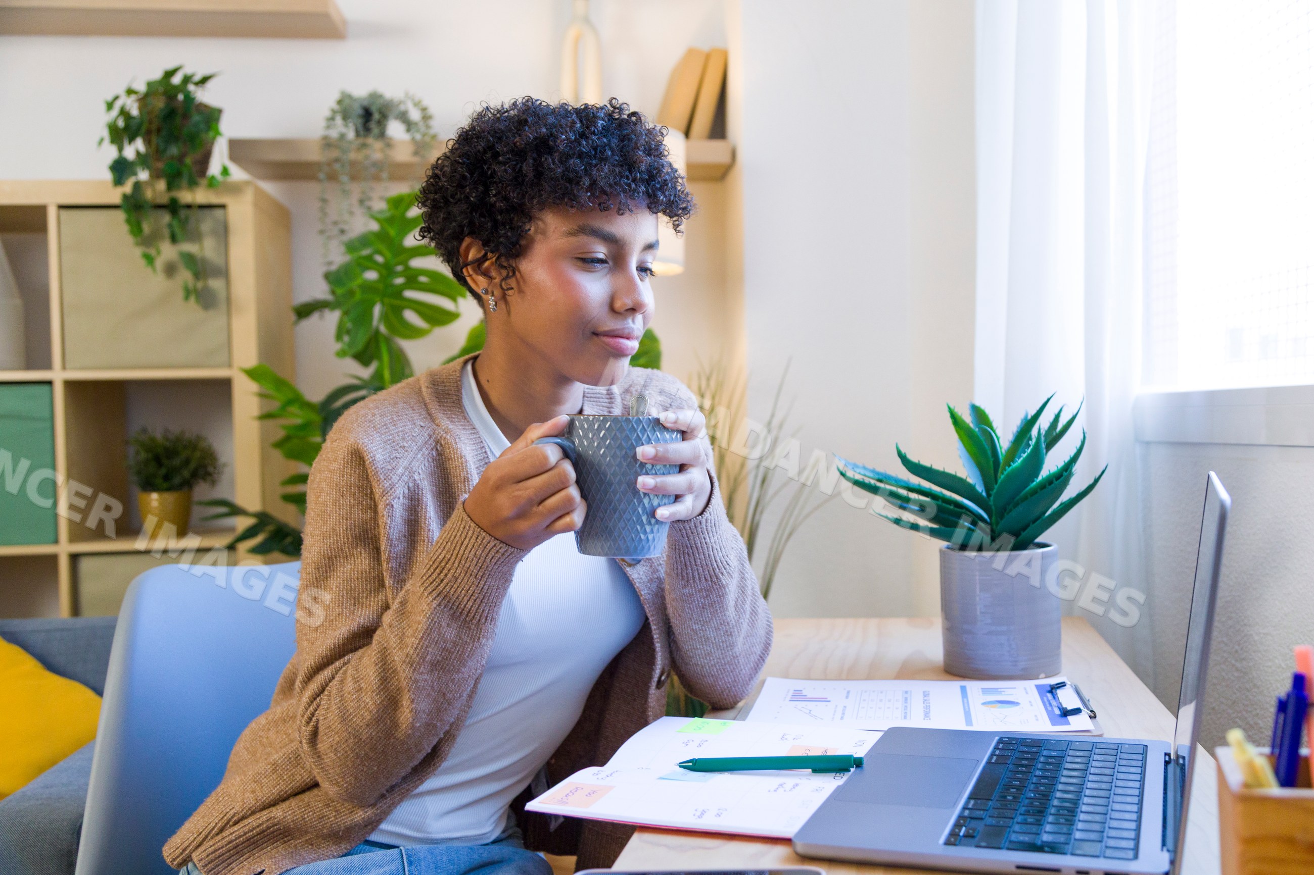 African American woman drinking coffee working on laptop