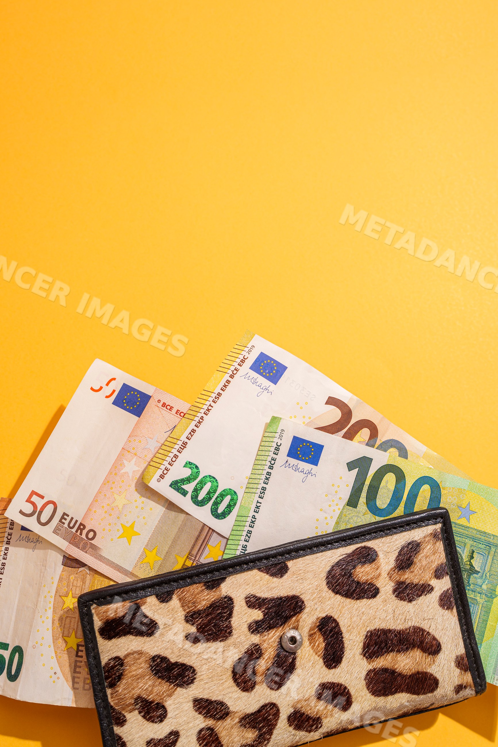 Leopard print wallet with euro banknotes on bright yellow background