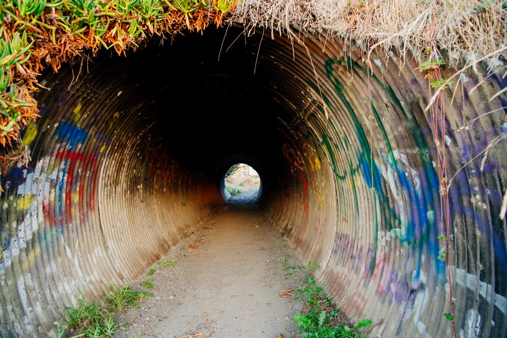 Graffiti-covered corrugated metal tunnel on dirt path in northern