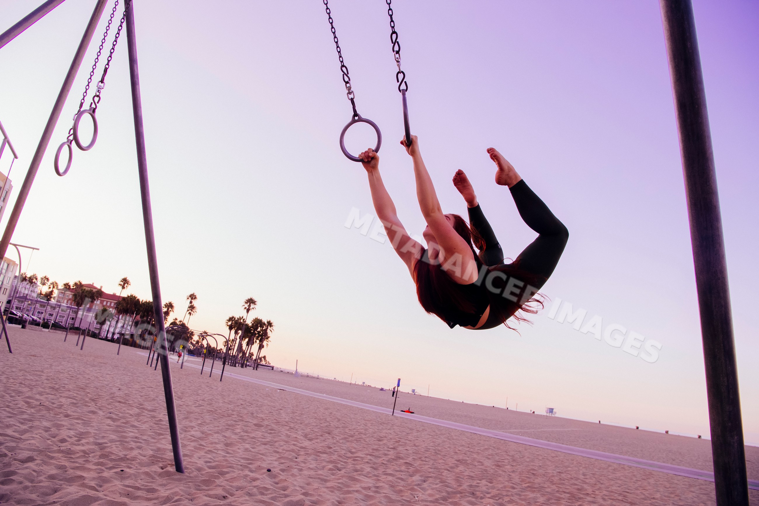 White woman exercising on gymnastics rings on California beach