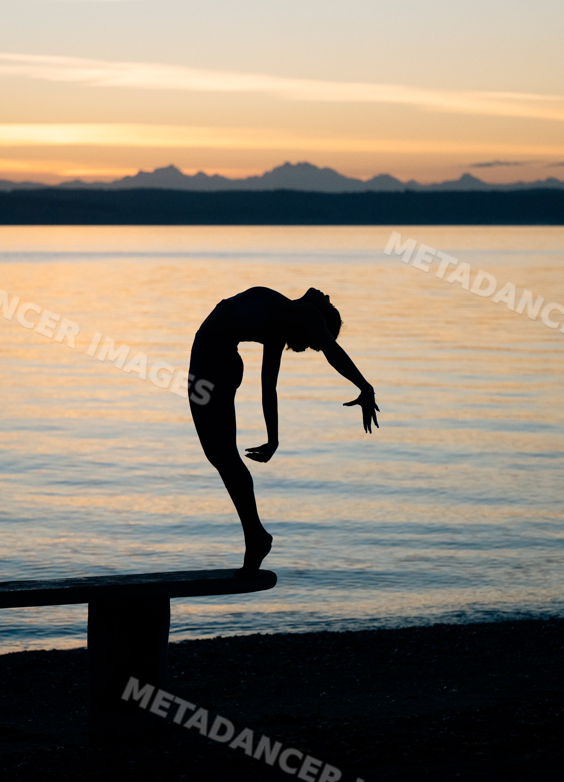 Hispanic woman balancing in a yoga acrobatics pose on a bench by water