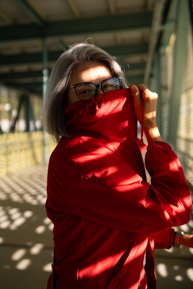White woman in red jacket smiling in sunlit outdoor corridor