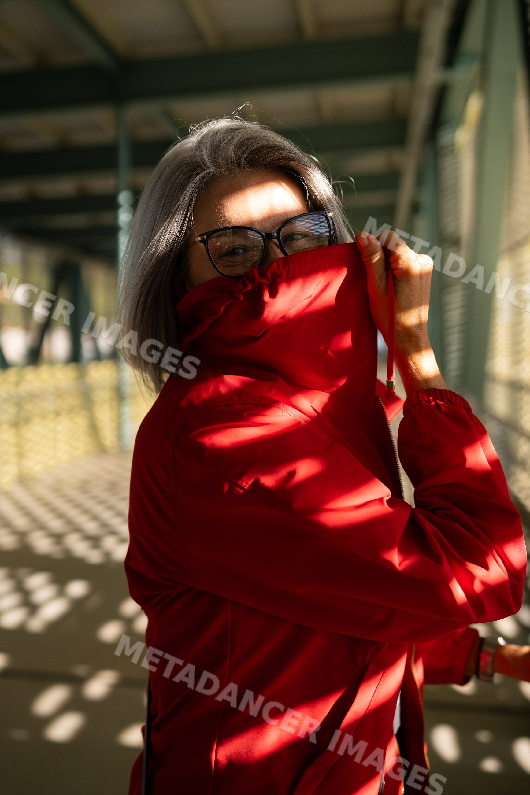 White woman in red jacket smiling in sunlit outdoor corridor