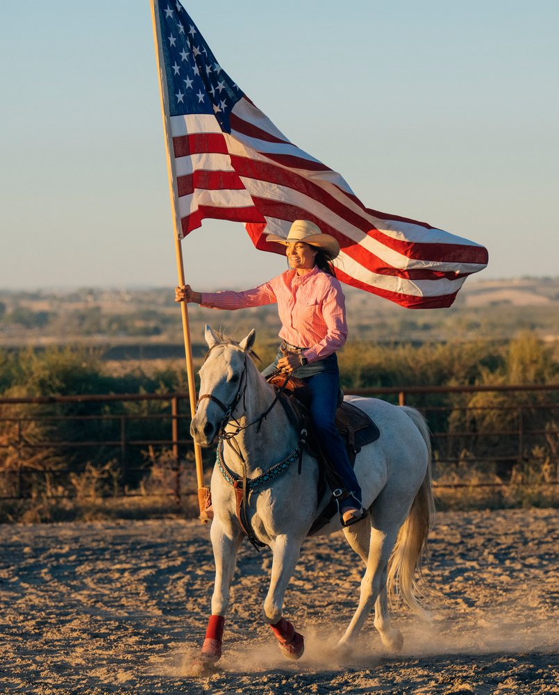 White woman riding horse holding american flag