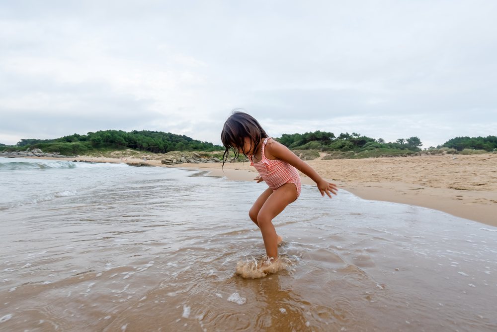 White child splashing water at sandy beach shoreline in a beach