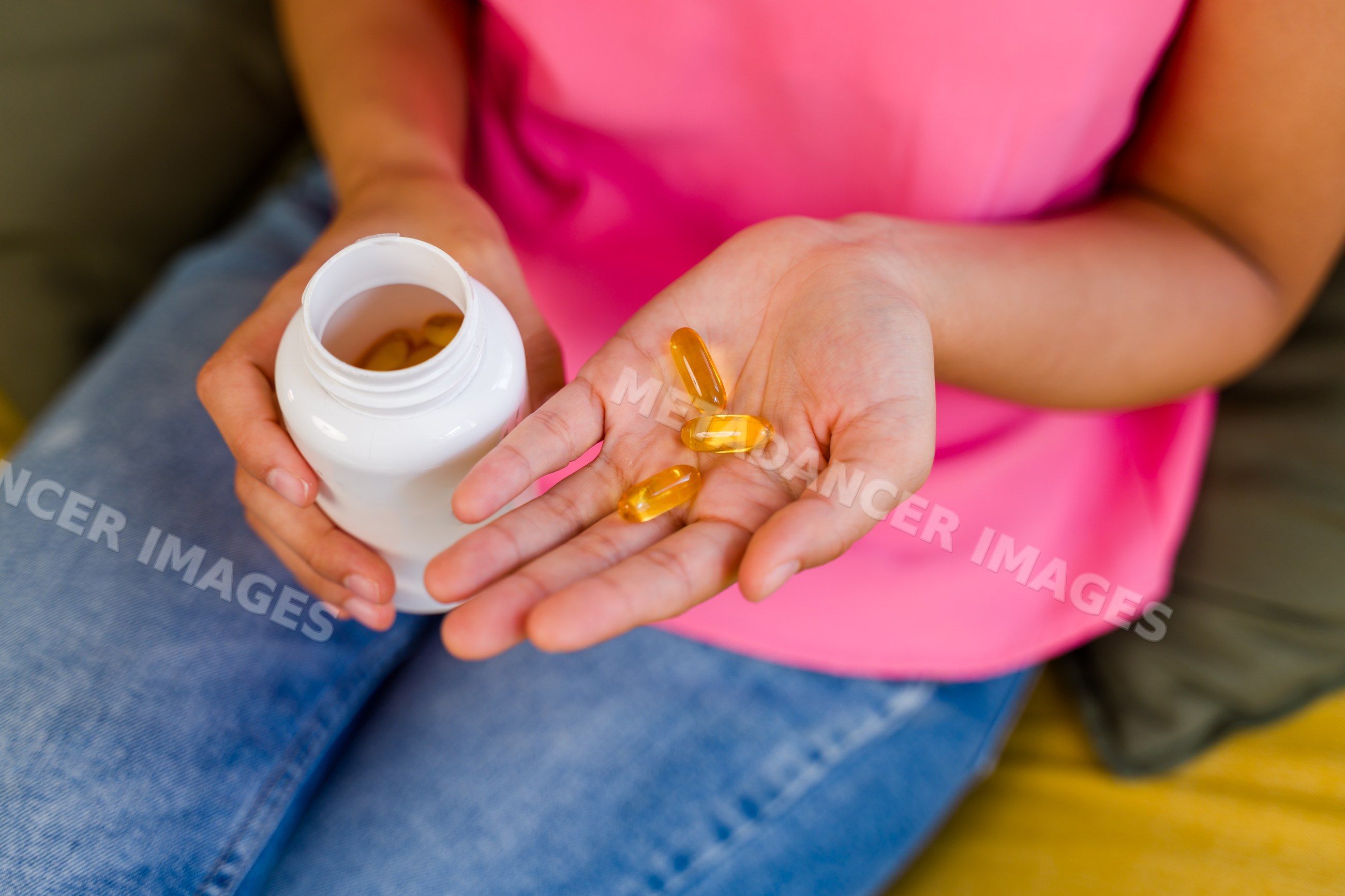 A Hispanic person holds yellow vitamin capsules and a supplement