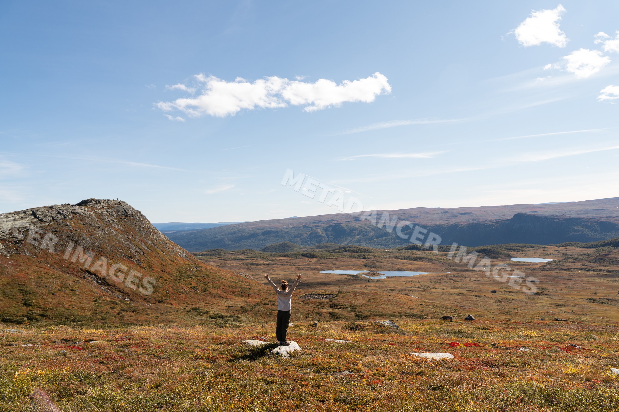Person standing on rock viewing scenic mountain valley and lakes