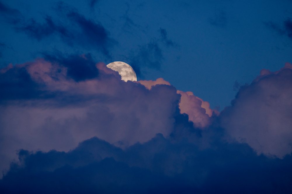 Full moon rising behind clouds in the evening sky