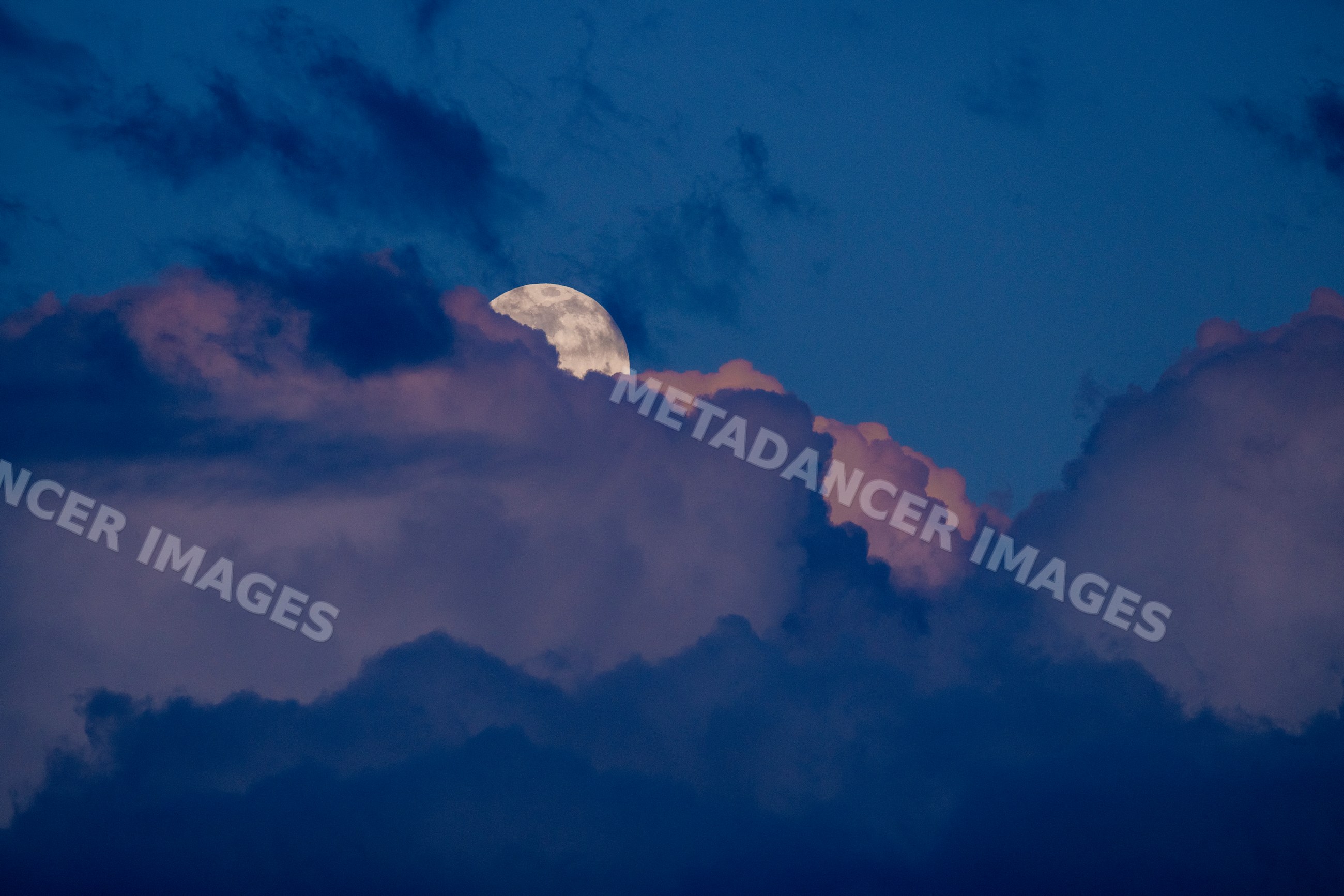 Full moon rising behind clouds in the evening sky