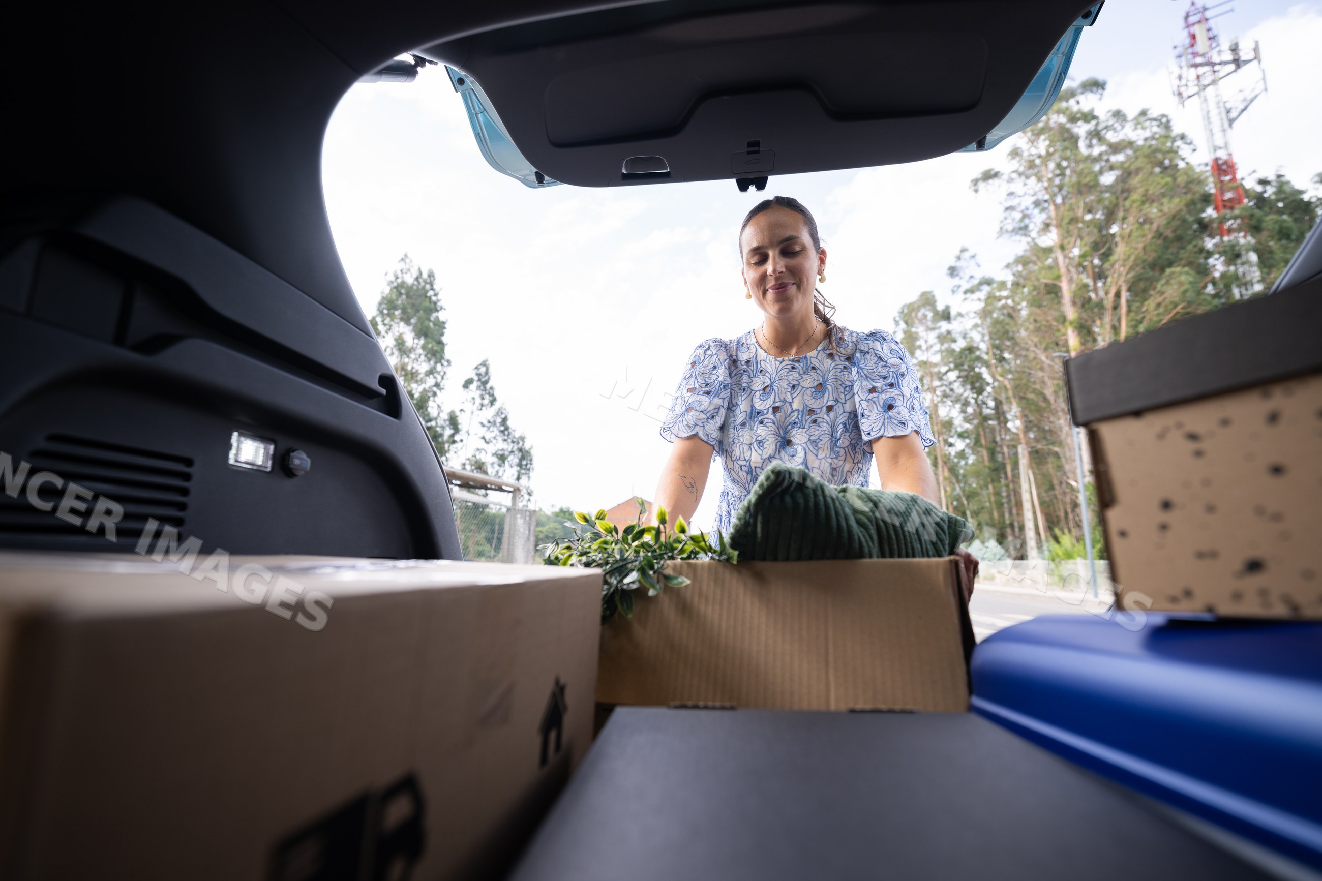 White woman unloading boxes from a car trunk outdoors
