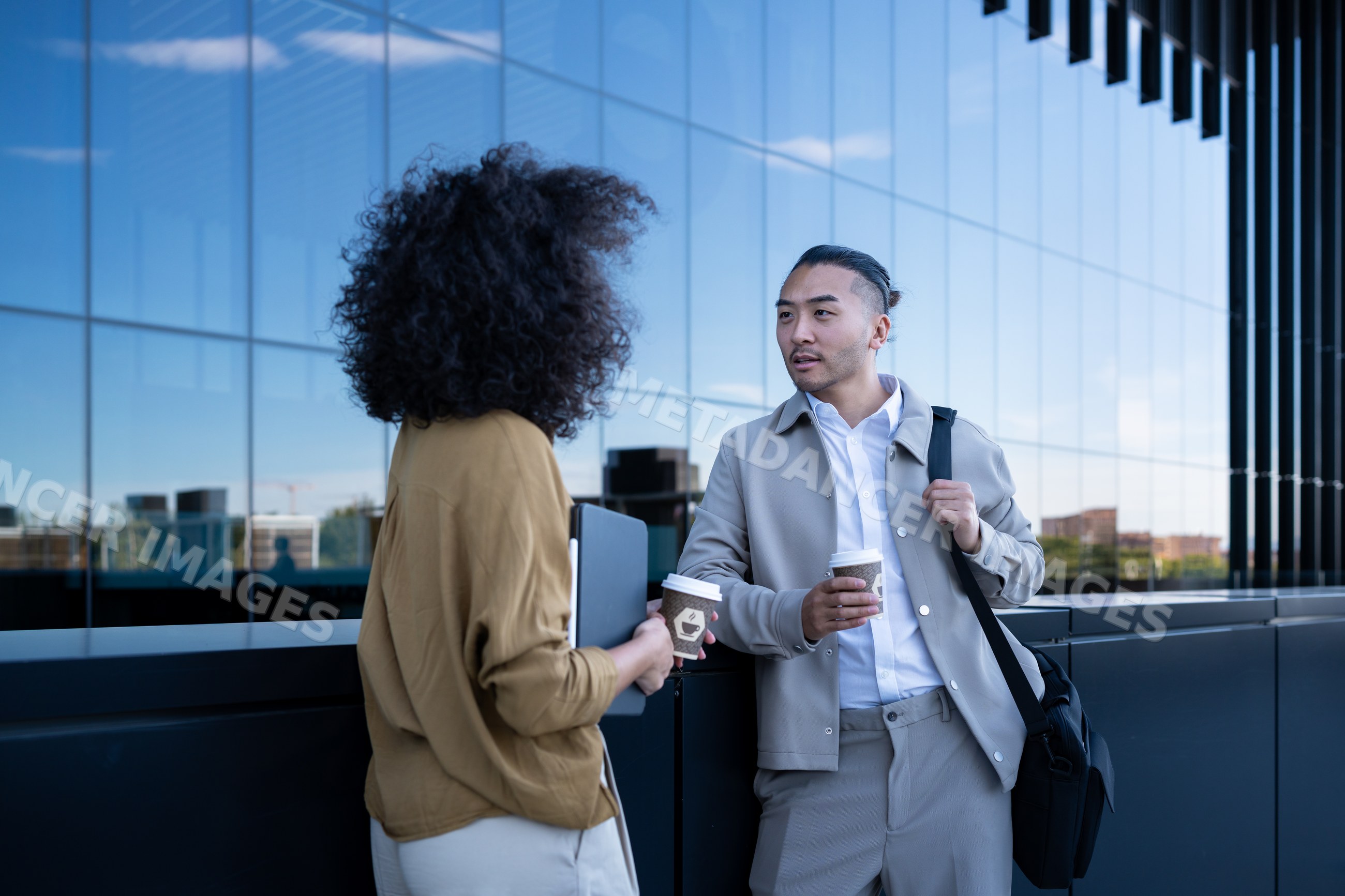 Two professionals conversing outdoors by office building with coffee