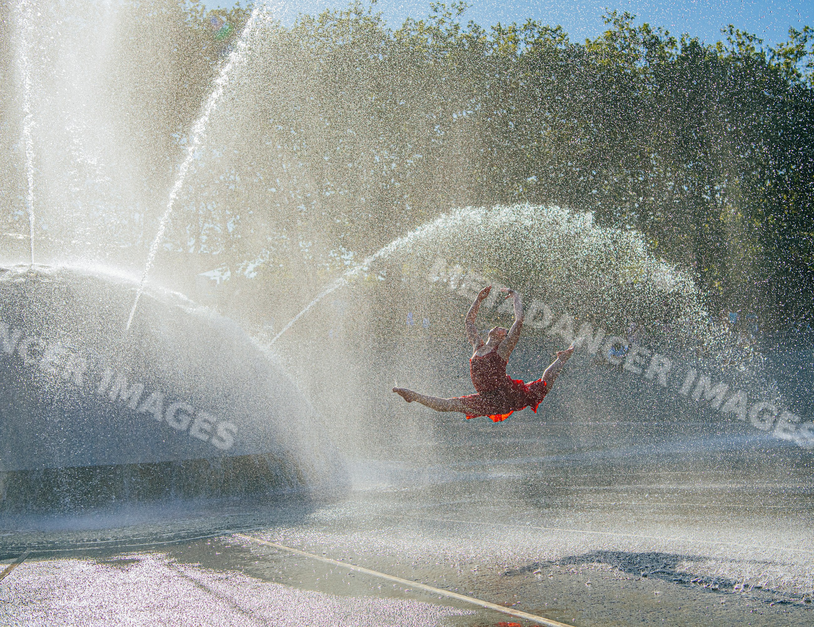 White dancer leaping through water sprays at outdoor fountain in USA