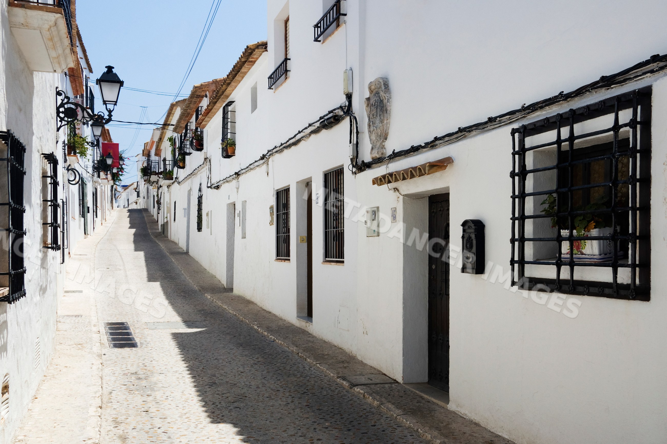 Narrow cobblestone street with white houses and balconies Spain