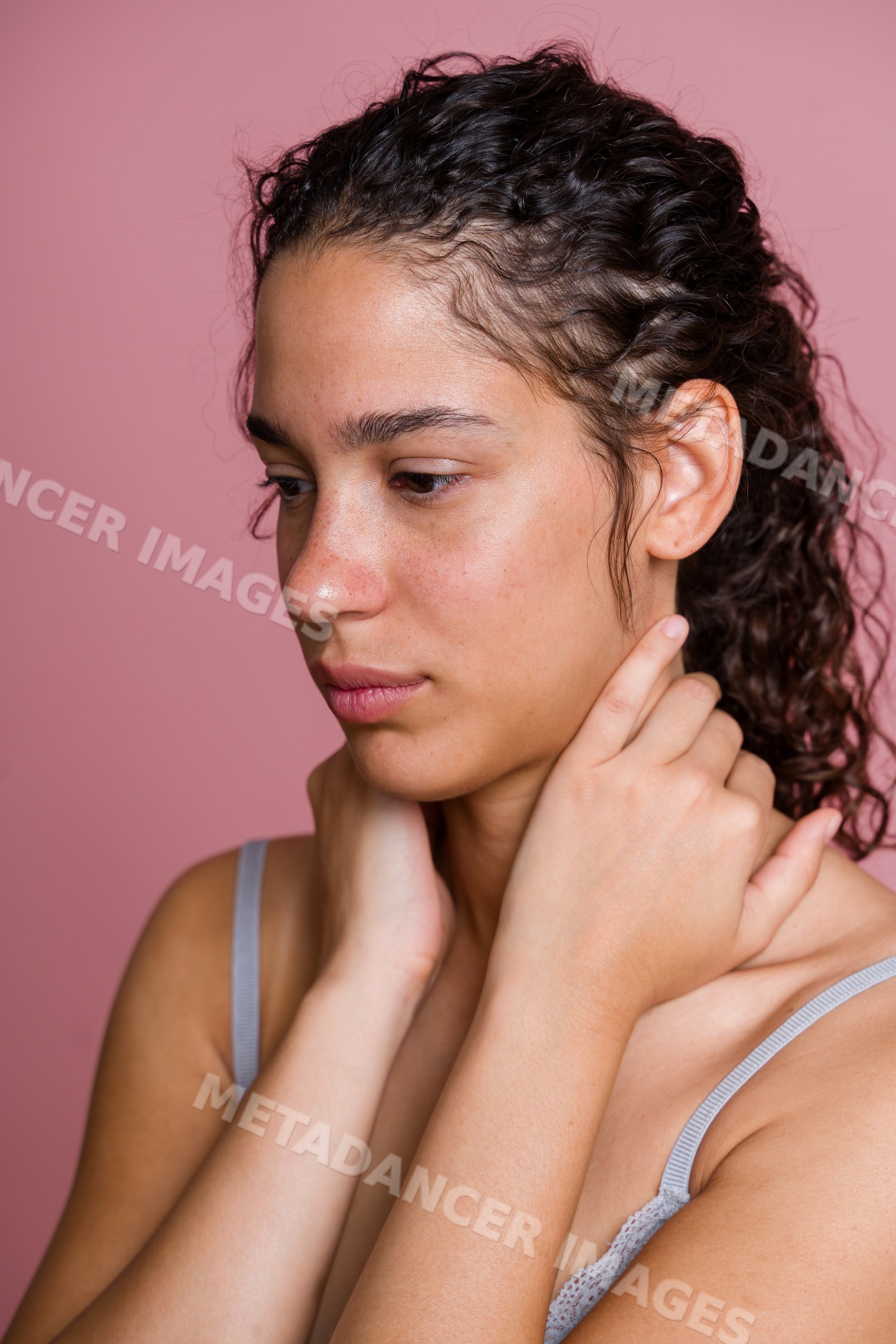 Hispanic woman with curly hair holding neck against pink background