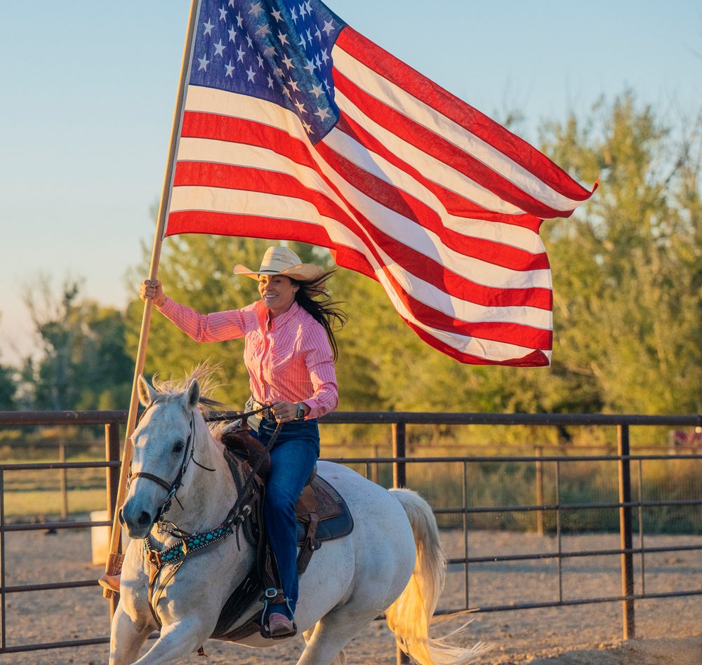 White woman riding horse carrying american flag