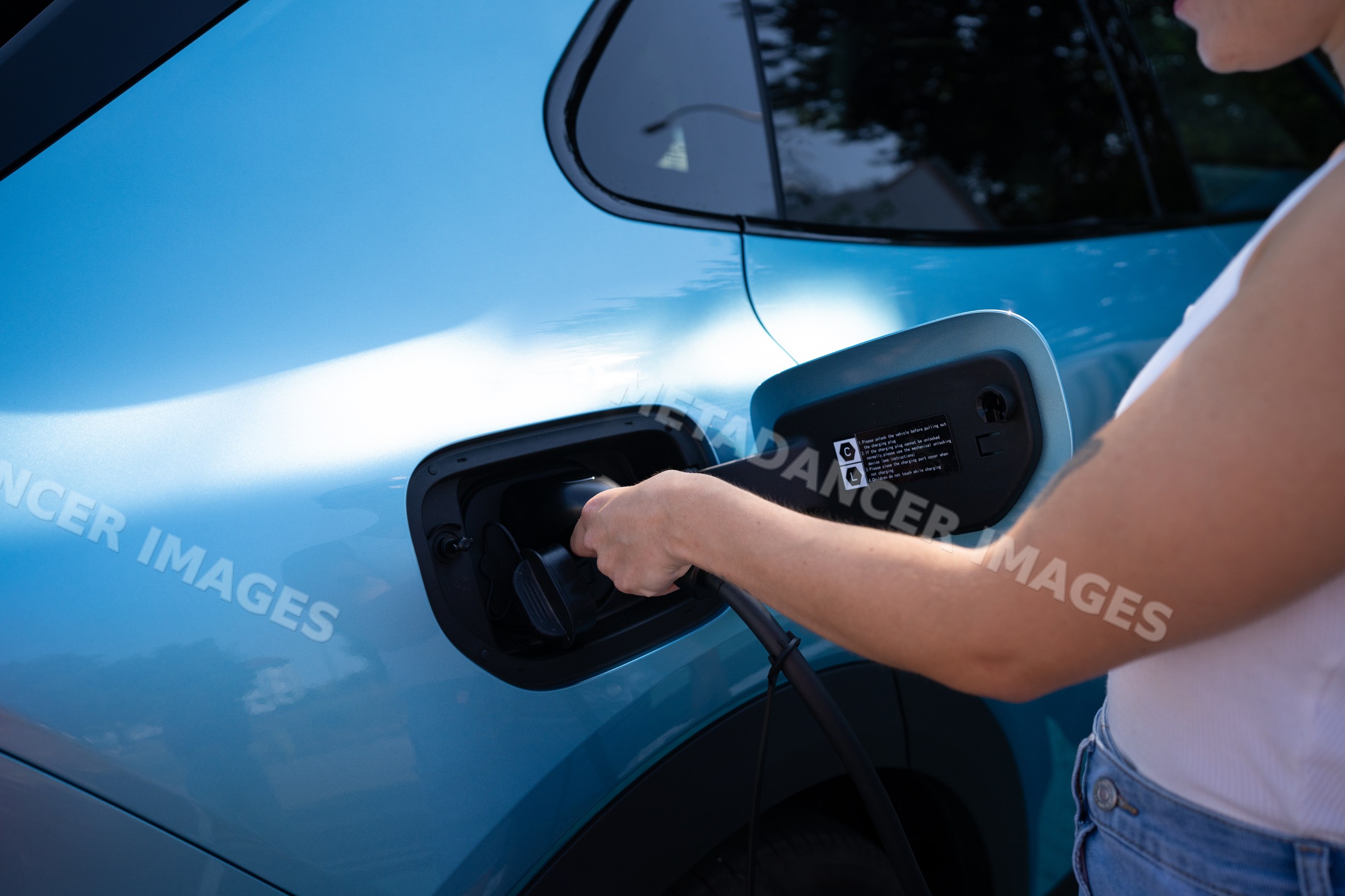 A white person charges an electric car with a cable