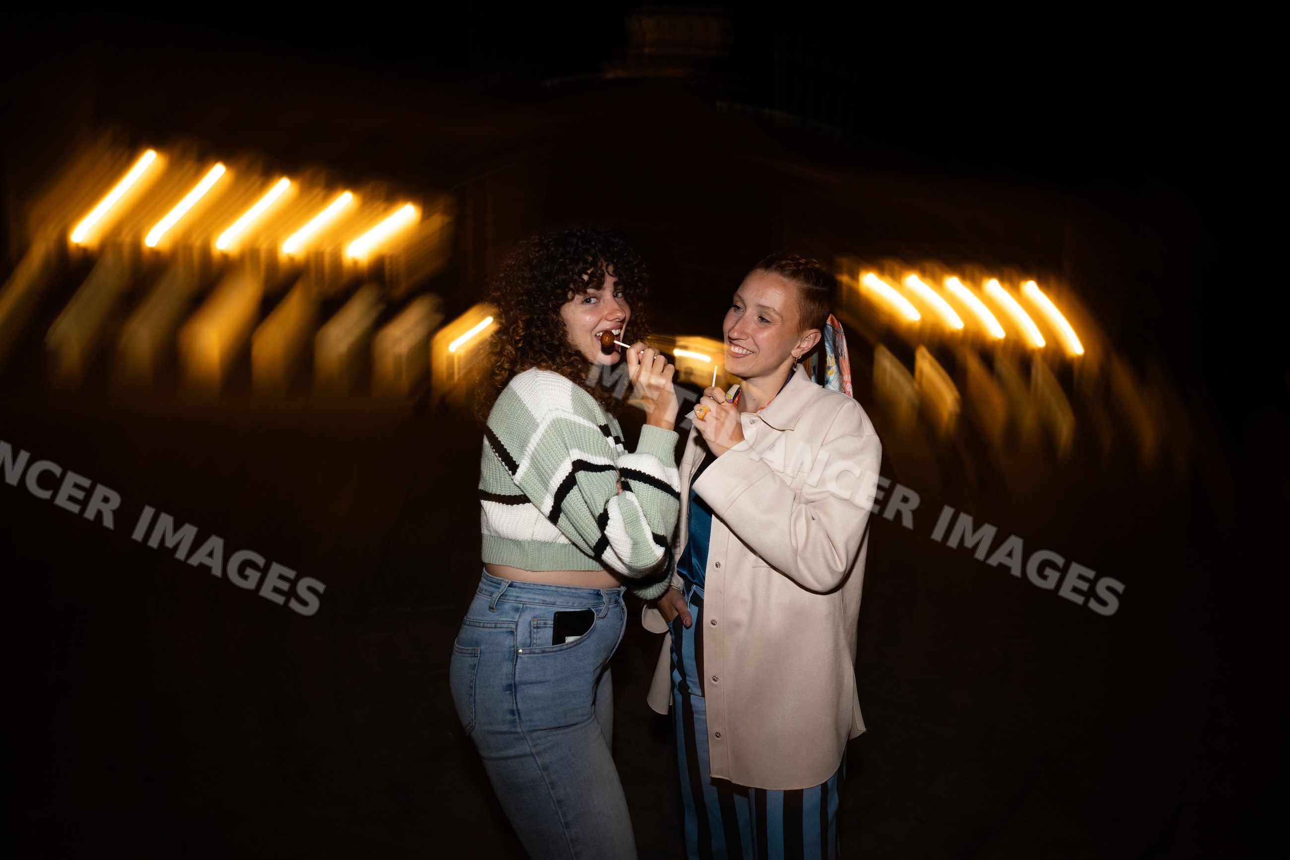 Two white women enjoying lollipops outdoors at night