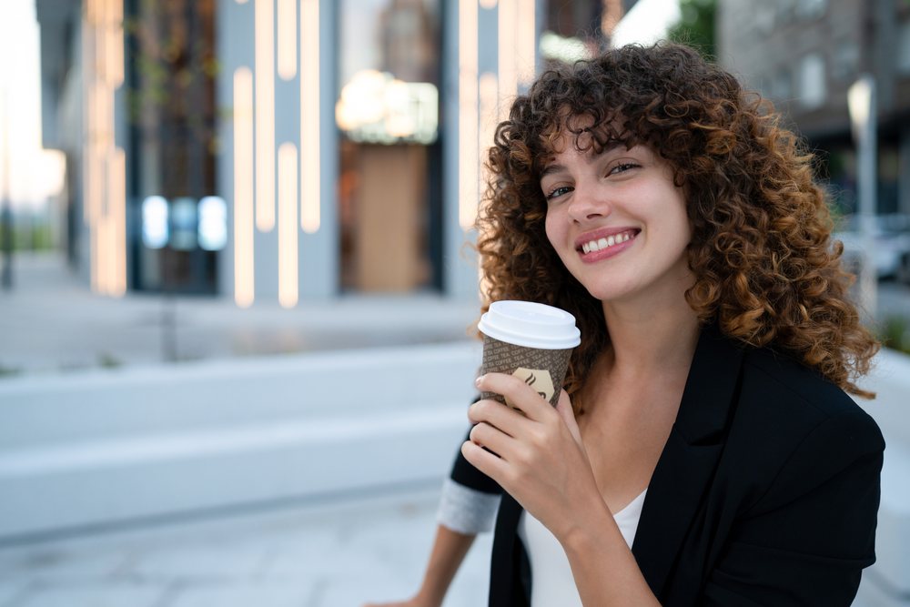 Young white woman holding coffee cup outdoors in Madrid urban setting