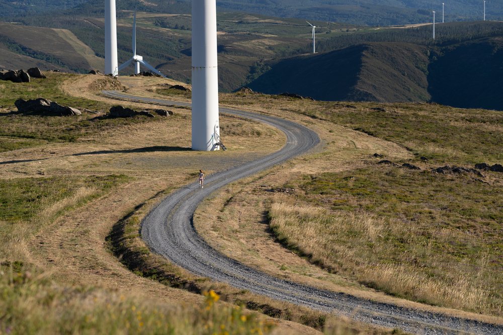 A white woman running on a trail by wind turbines in Galicia, Spain