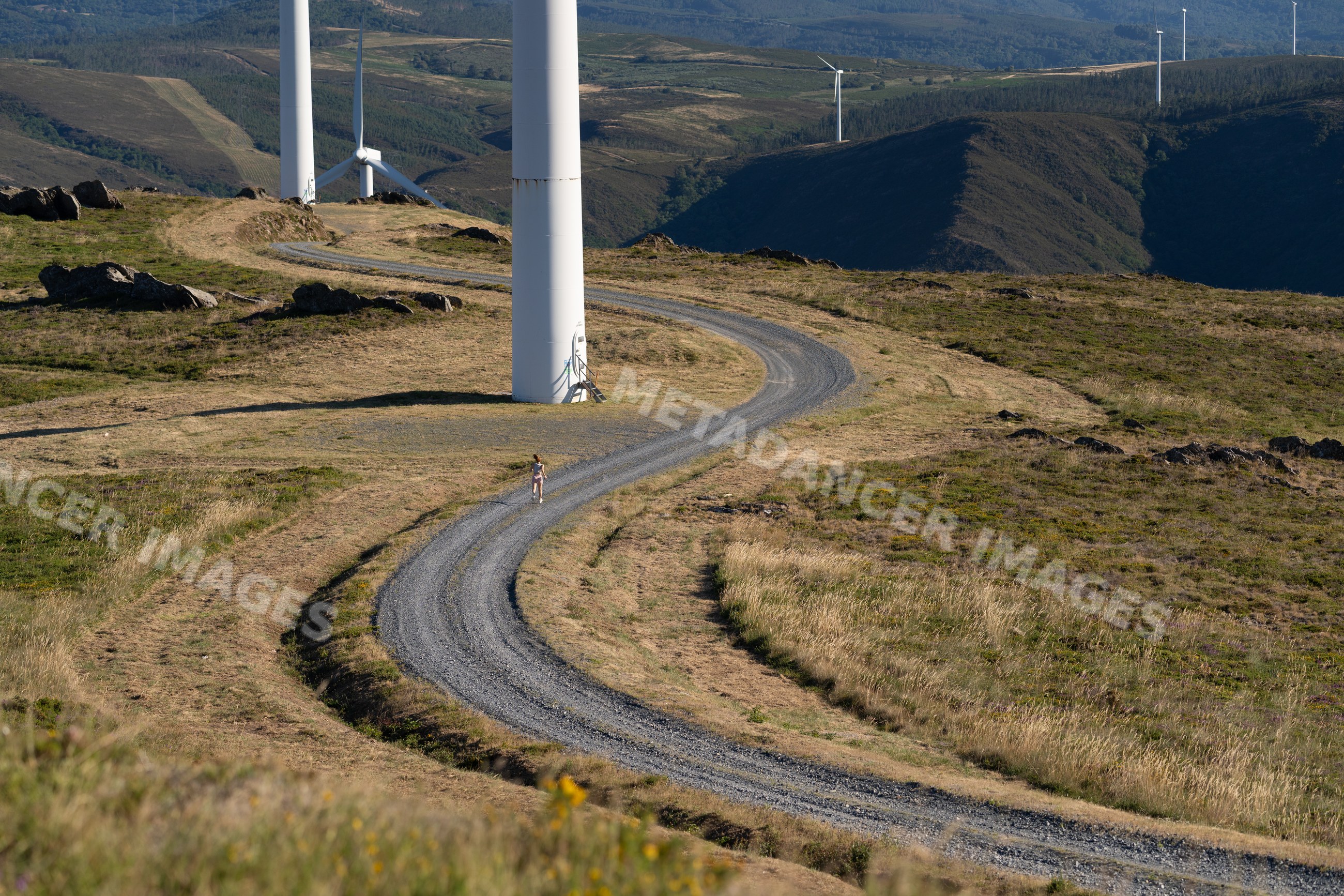 A white woman running on a trail by wind turbines in Galicia, Spain