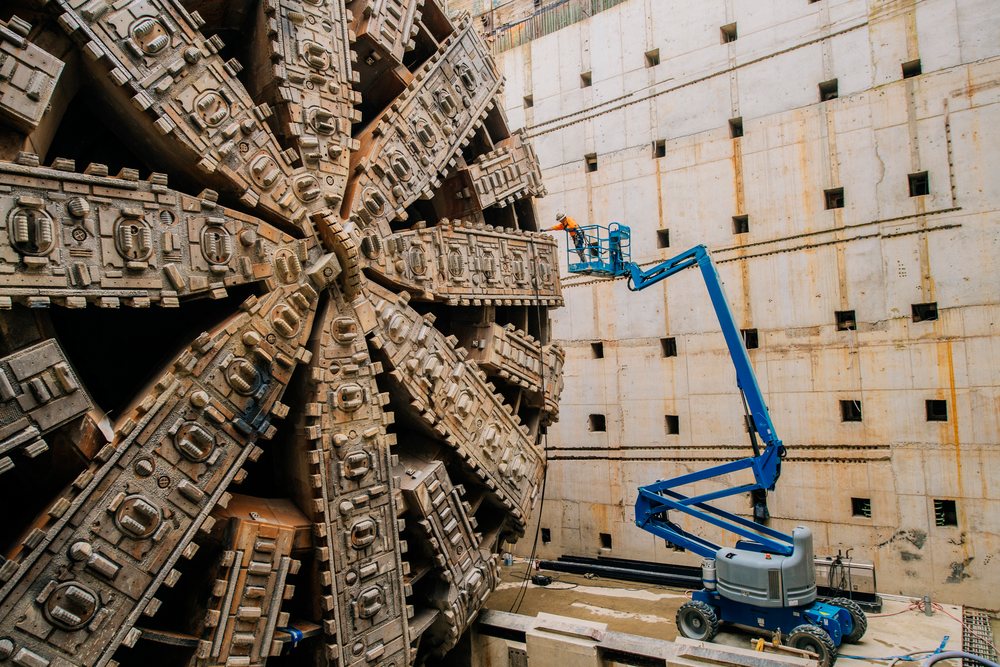 Worker inspects massive tunnel boring machine at construction site
