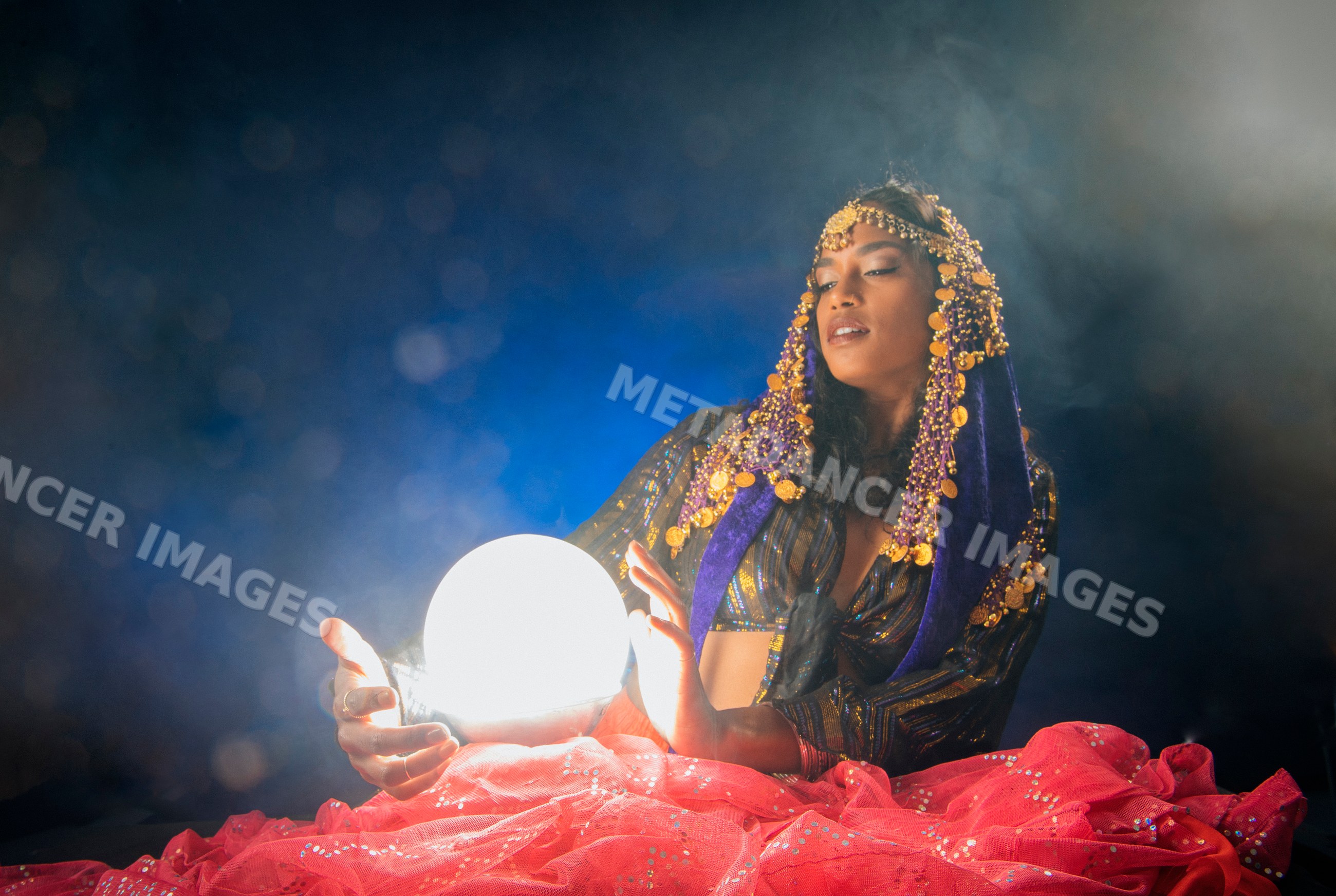 A South Asian woman holds a glowing crystal ball wearing mystical