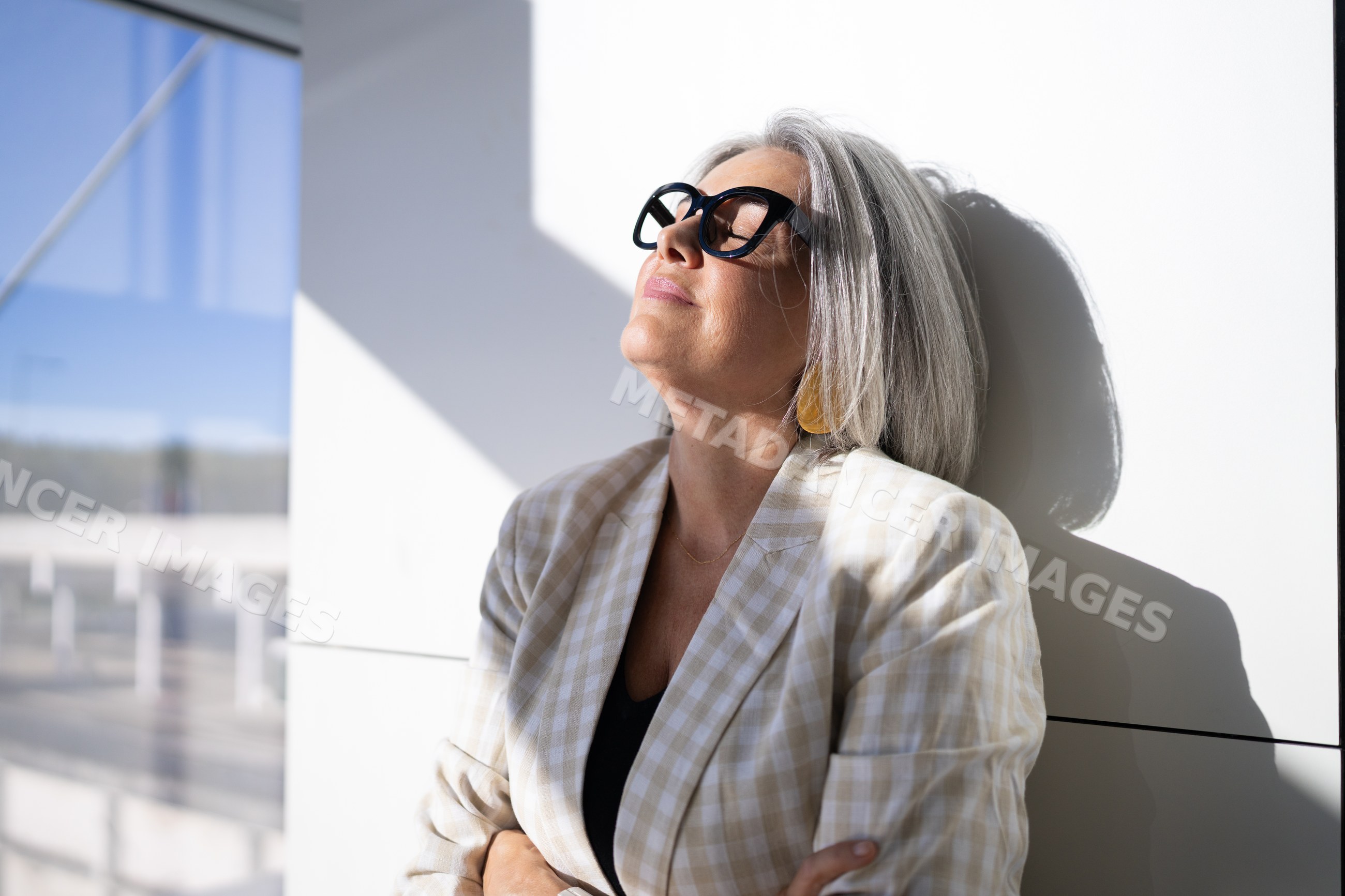 Mature white woman enjoying sunlight against wall