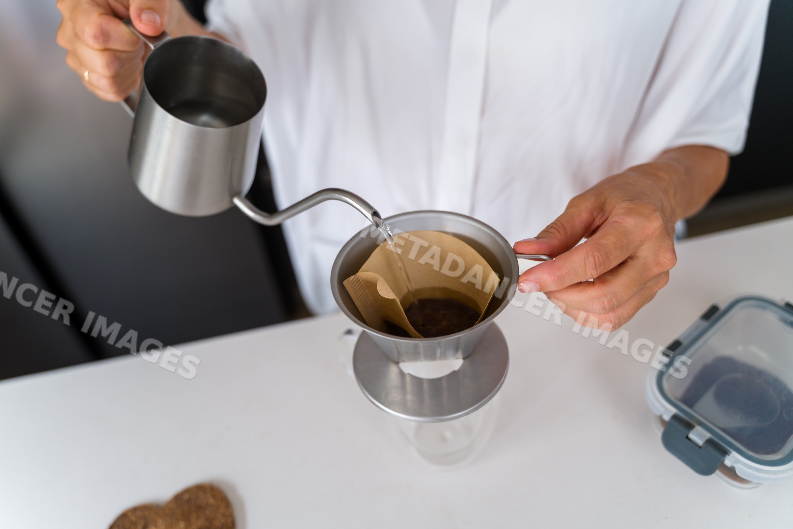 Pouring water for coffee brewing with metal dripper in kitchen