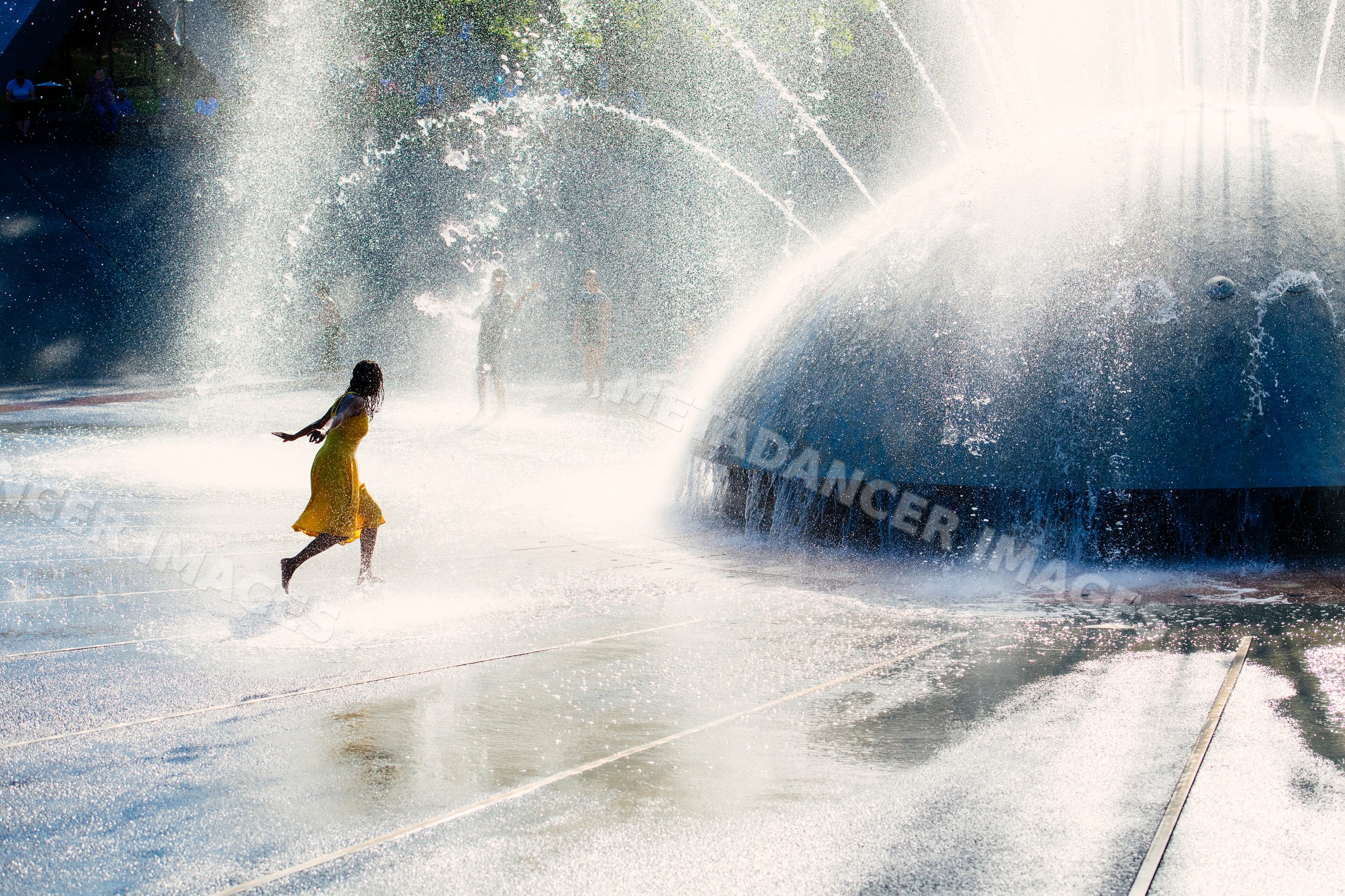 South Asian woman running through water spray of large outdoor