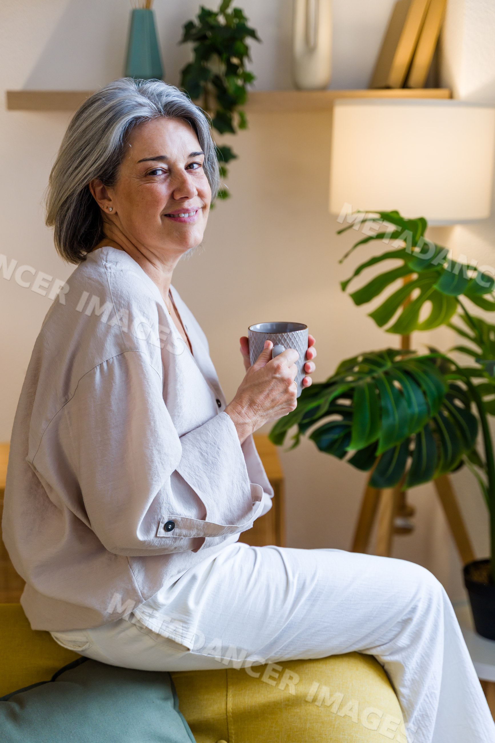 Middle-aged white woman holding mug sitting on yellow couch