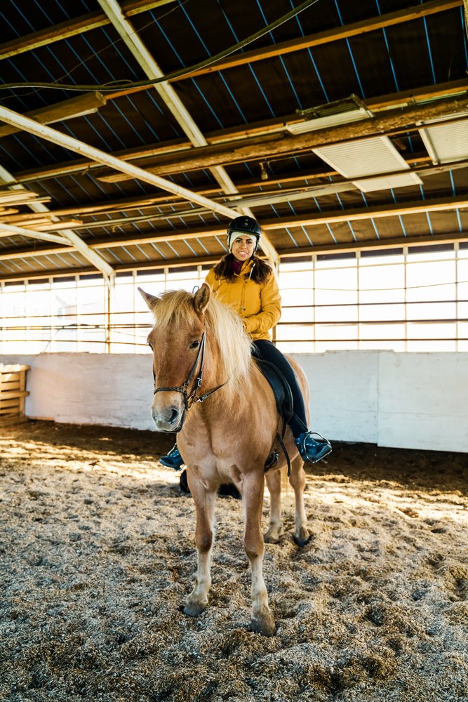 A white woman rides a horse in an indoor riding arena