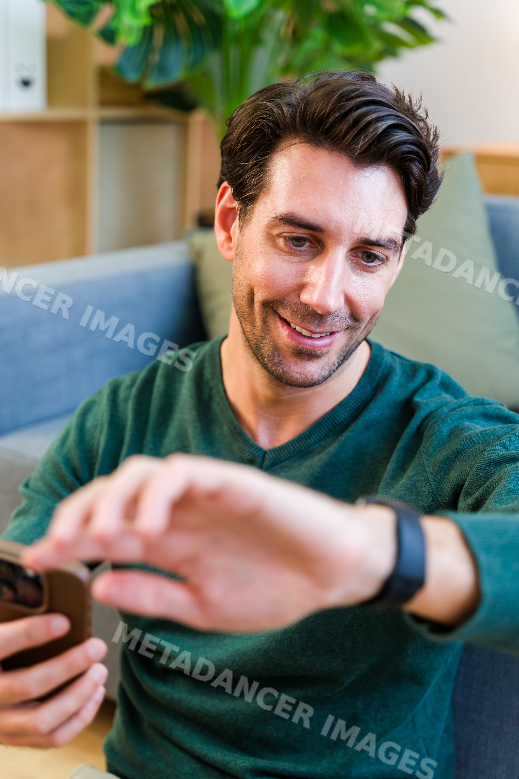 White man checking smartwatch while sitting on couch in living room