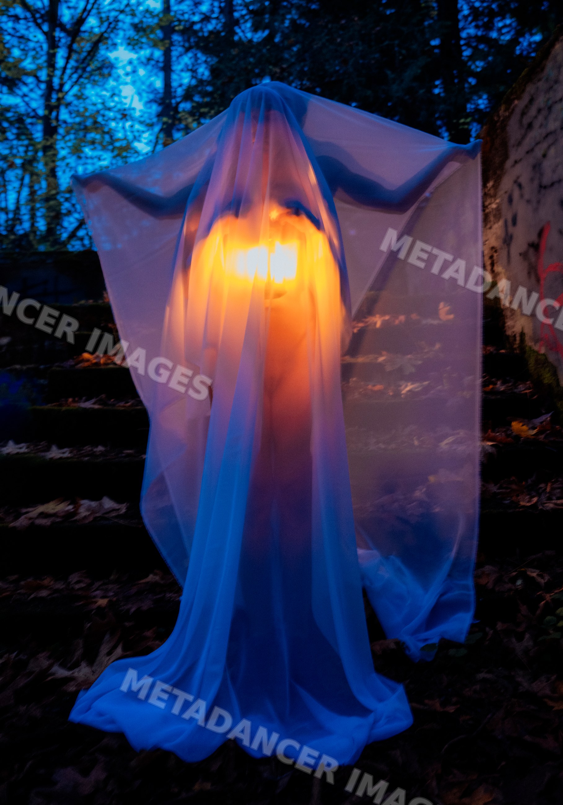 Ghost figure glowing under white sheet outdoors at night